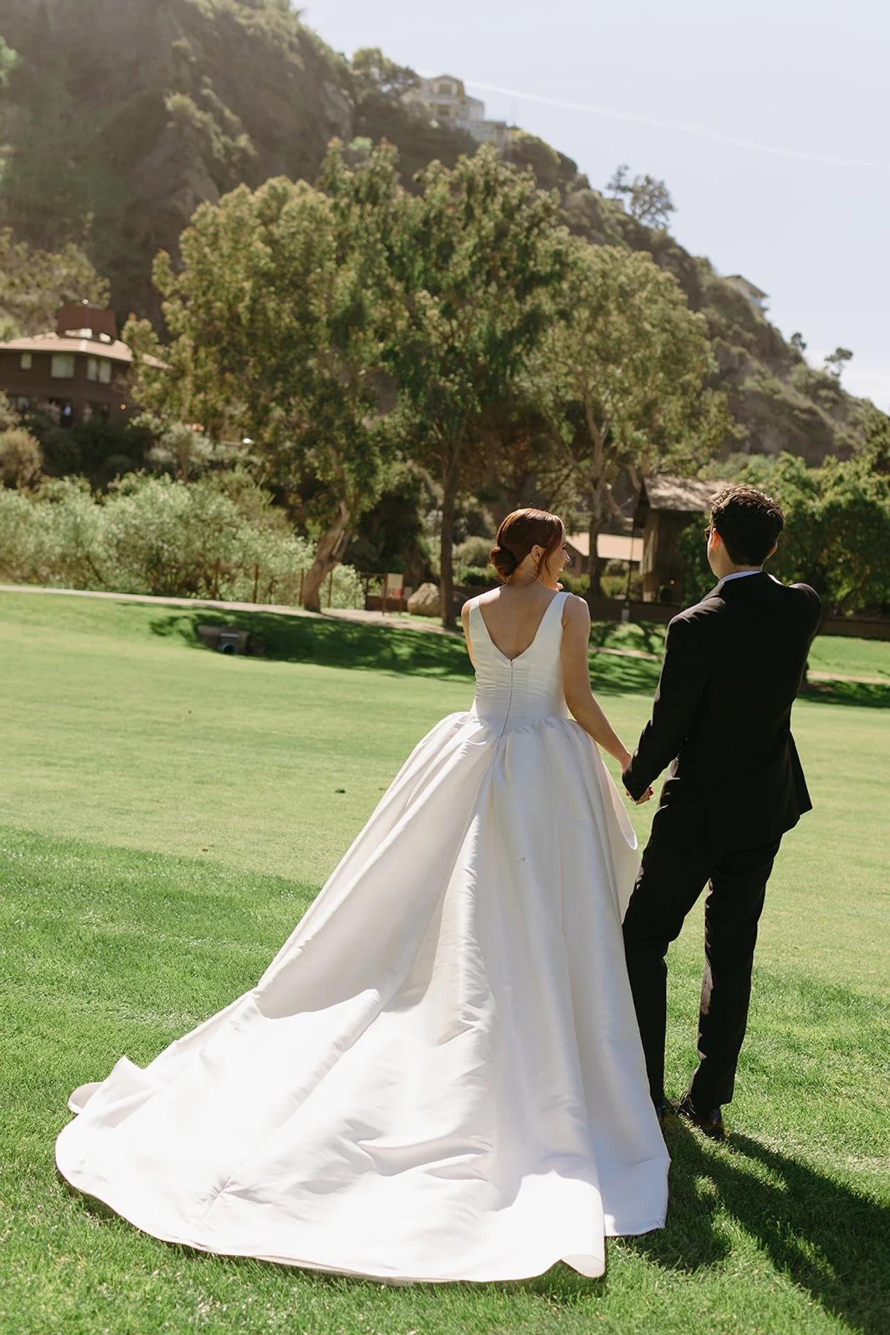 Bride and groom walking hand in hand across the golf course with the bride’s long train flowing behind her.