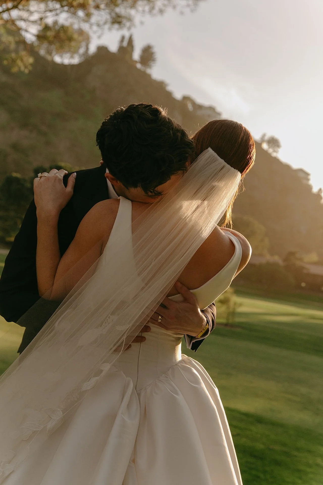 Bride and groom embracing during golden hour portraits with canyon hills glowing behind them at The Ranch at Laguna Beach wedding.