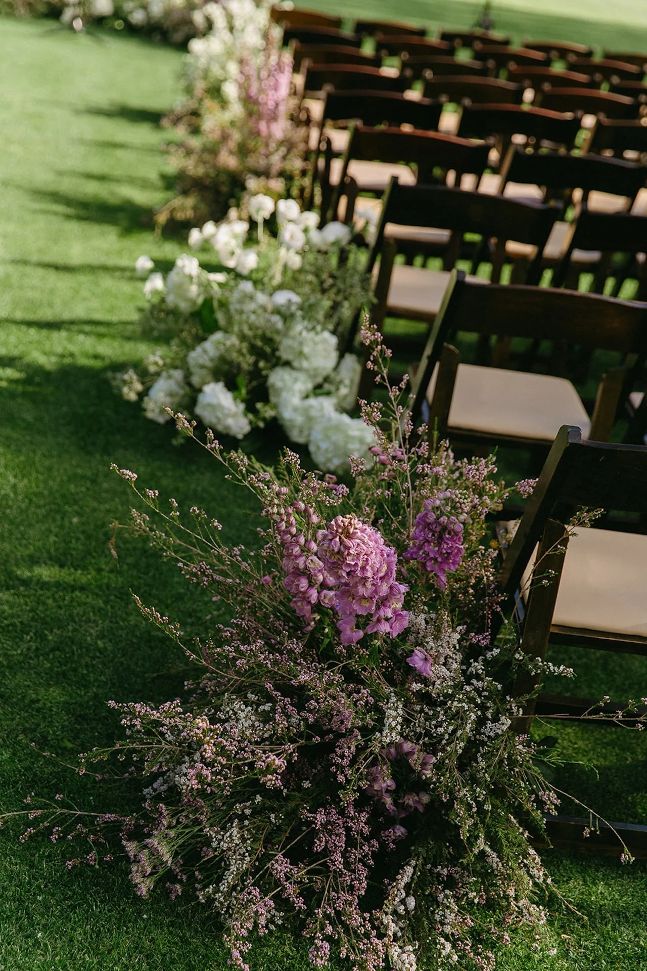 Ceremony aisle lined with organic floral arrangements in blush and white tones leading to an outdoor wedding altar on the lawn.