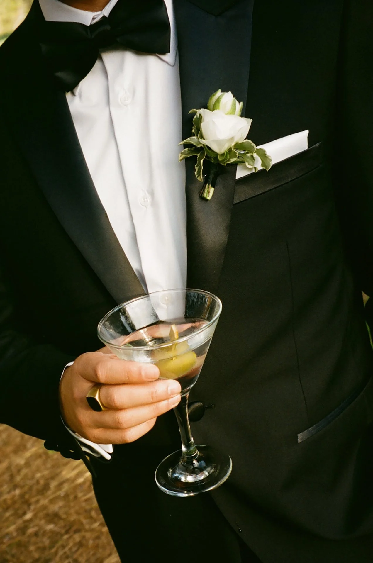 Close up of groom in a classic black tuxedo holding a martini with boutonniere detail at The Ranch at Laguna Beach wedding cocktail hour.