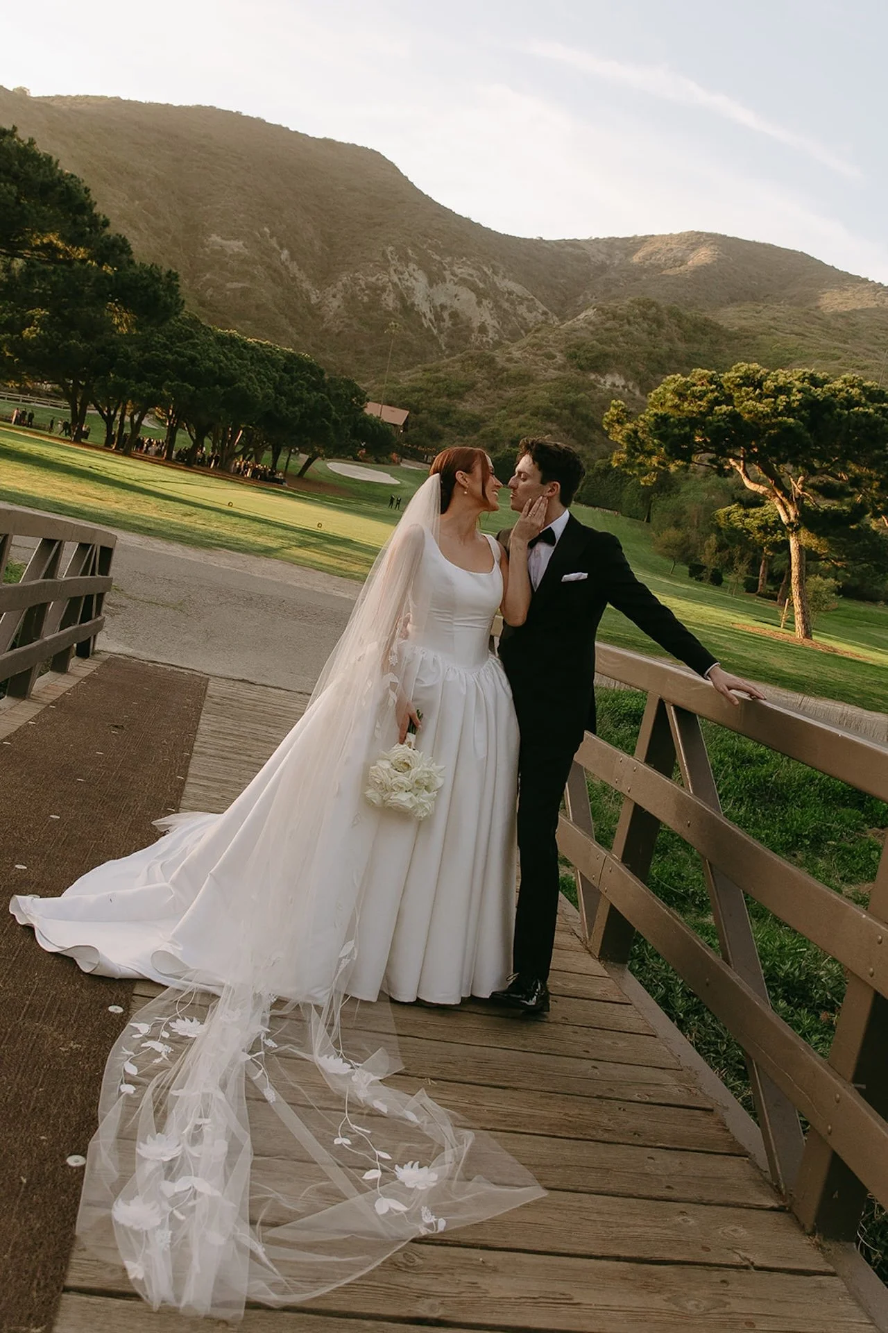 Bride and groom sharing a kiss on the wooden bridge with mountain views behind them.