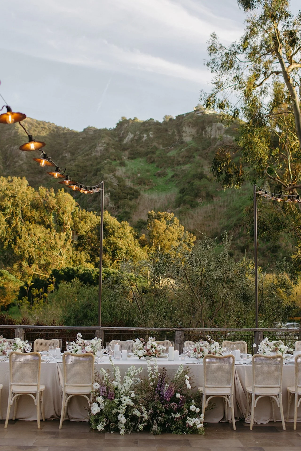 Outdoor reception tablescape with neutral linens, rattan chairs, and lush floral arrangements beneath string lights at The Ranch at Laguna Beach wedding.