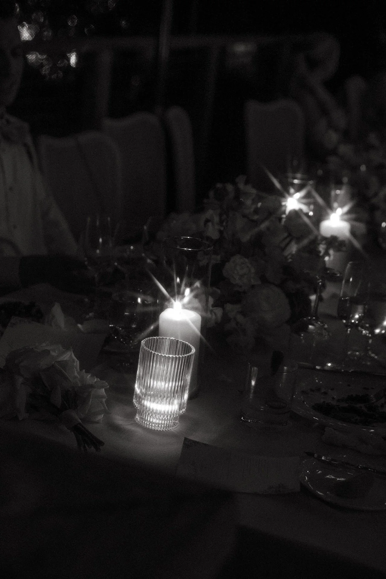 Moody evening reception table details featuring glowing candles, glassware, and romantic low light ambiance.