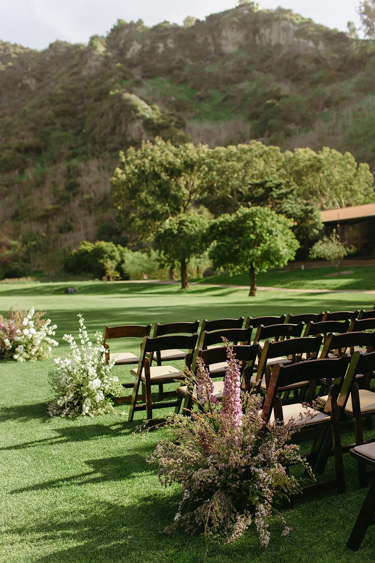 Outdoor ceremony aisle with dark wooden chairs and floral arrangements lining the lawn.