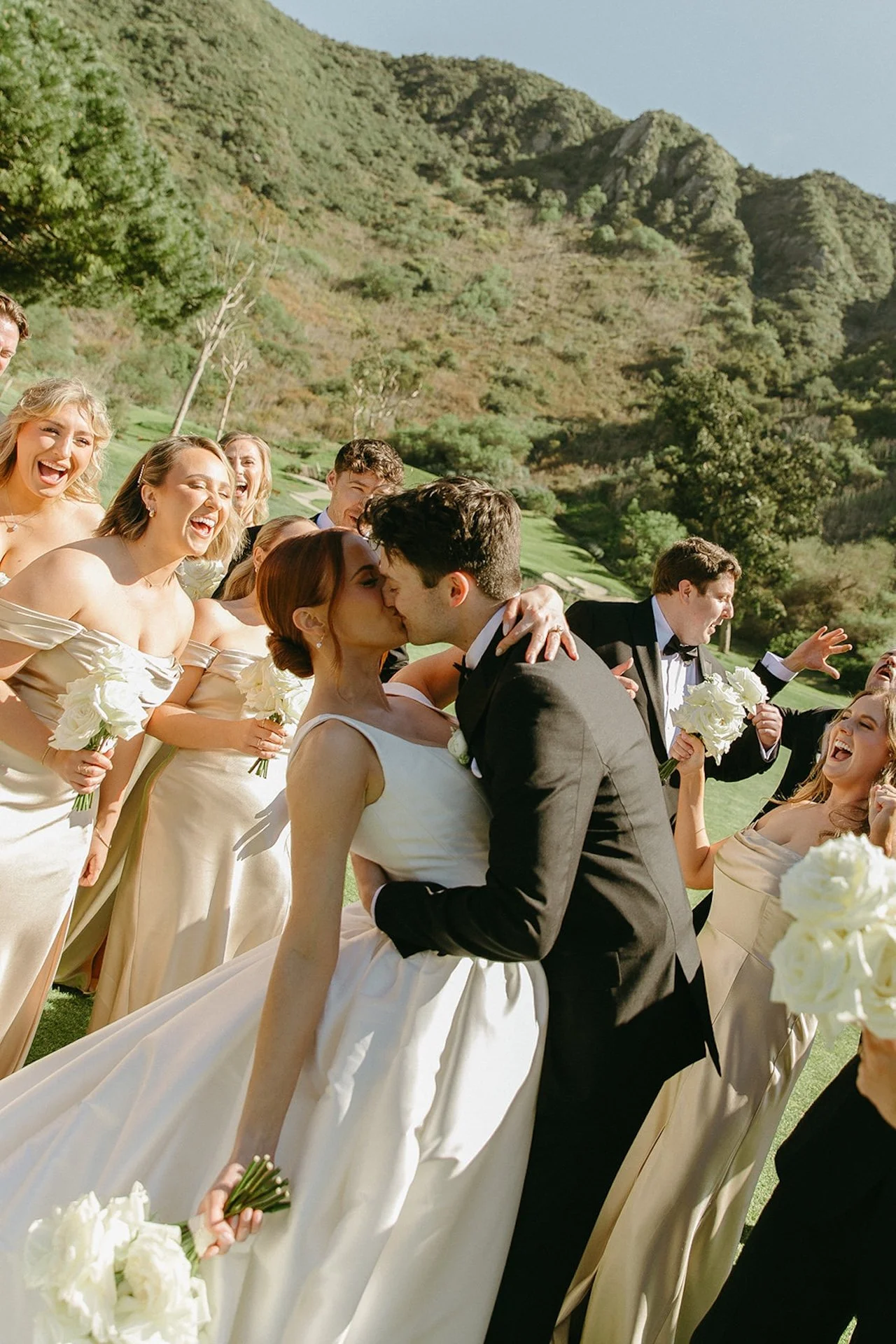 Bride and groom kissing surrounded by their wedding party on the golf course lawn at The Ranch at Laguna Beach wedding.