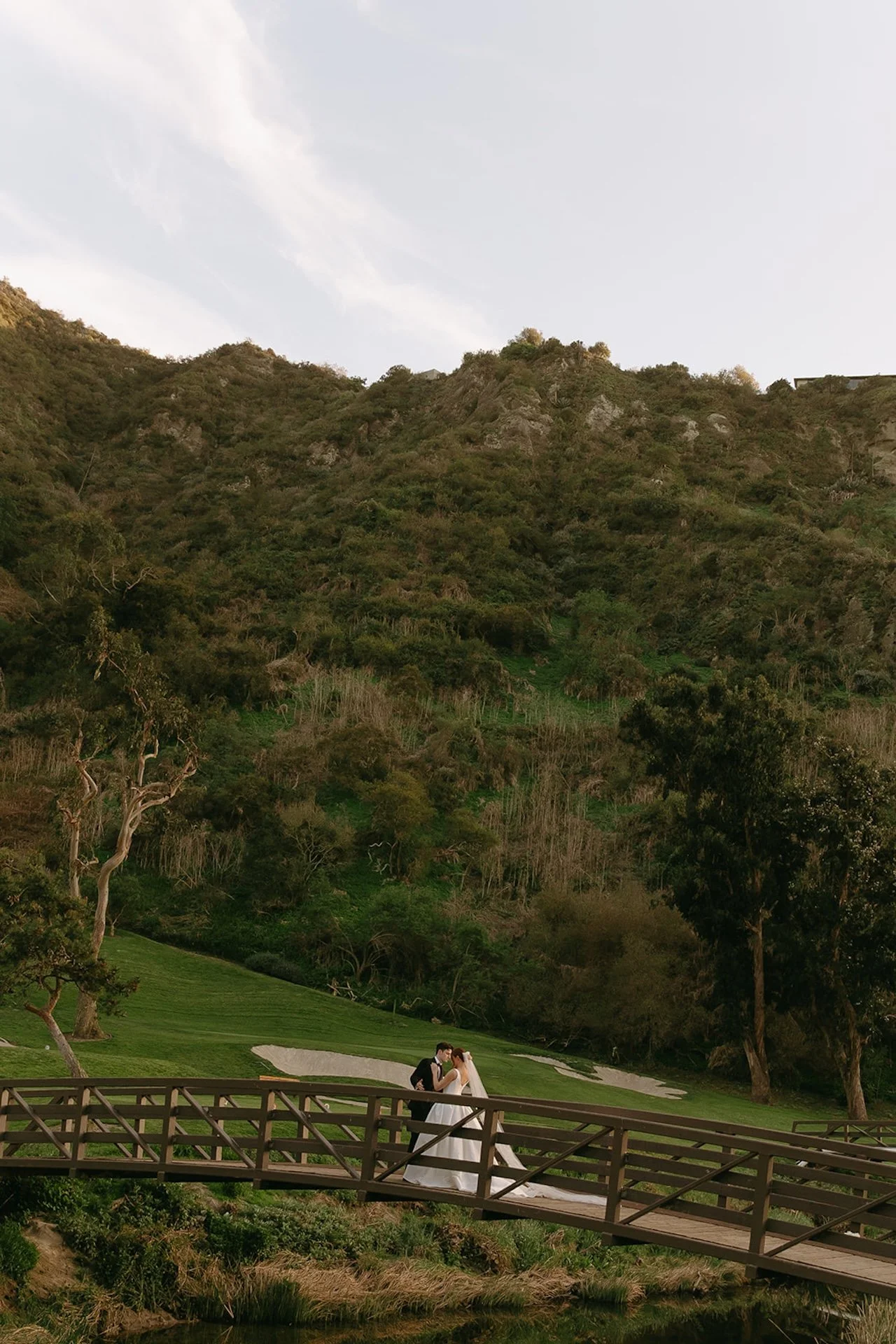Bride and groom standing on the wooden bridge surrounded by canyon hills at The Ranch at Laguna Beach wedding venue.