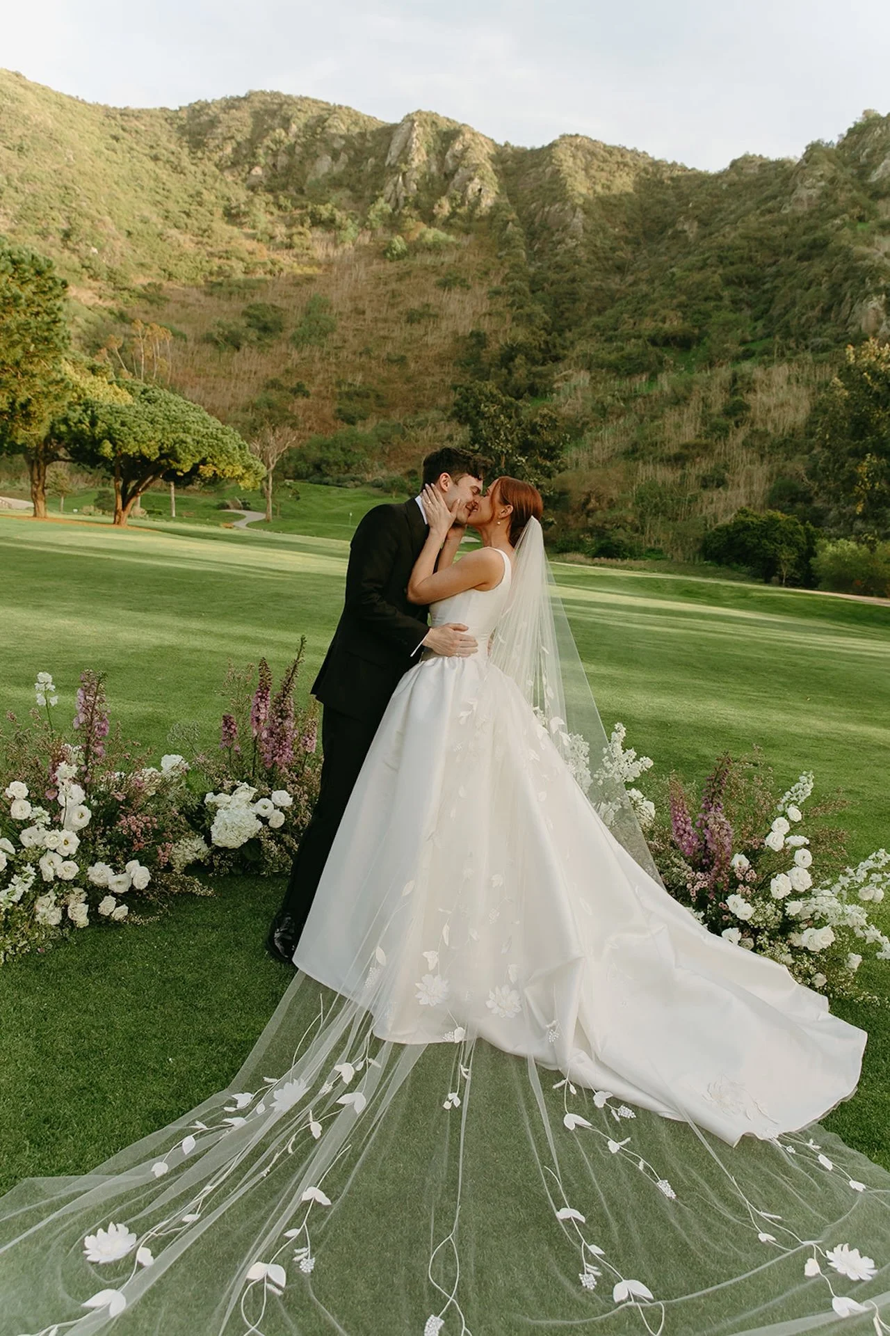 Bride and groom kissing in front of floral arrangements on the canyon lawn at The Ranch at Laguna Beach wedding.
