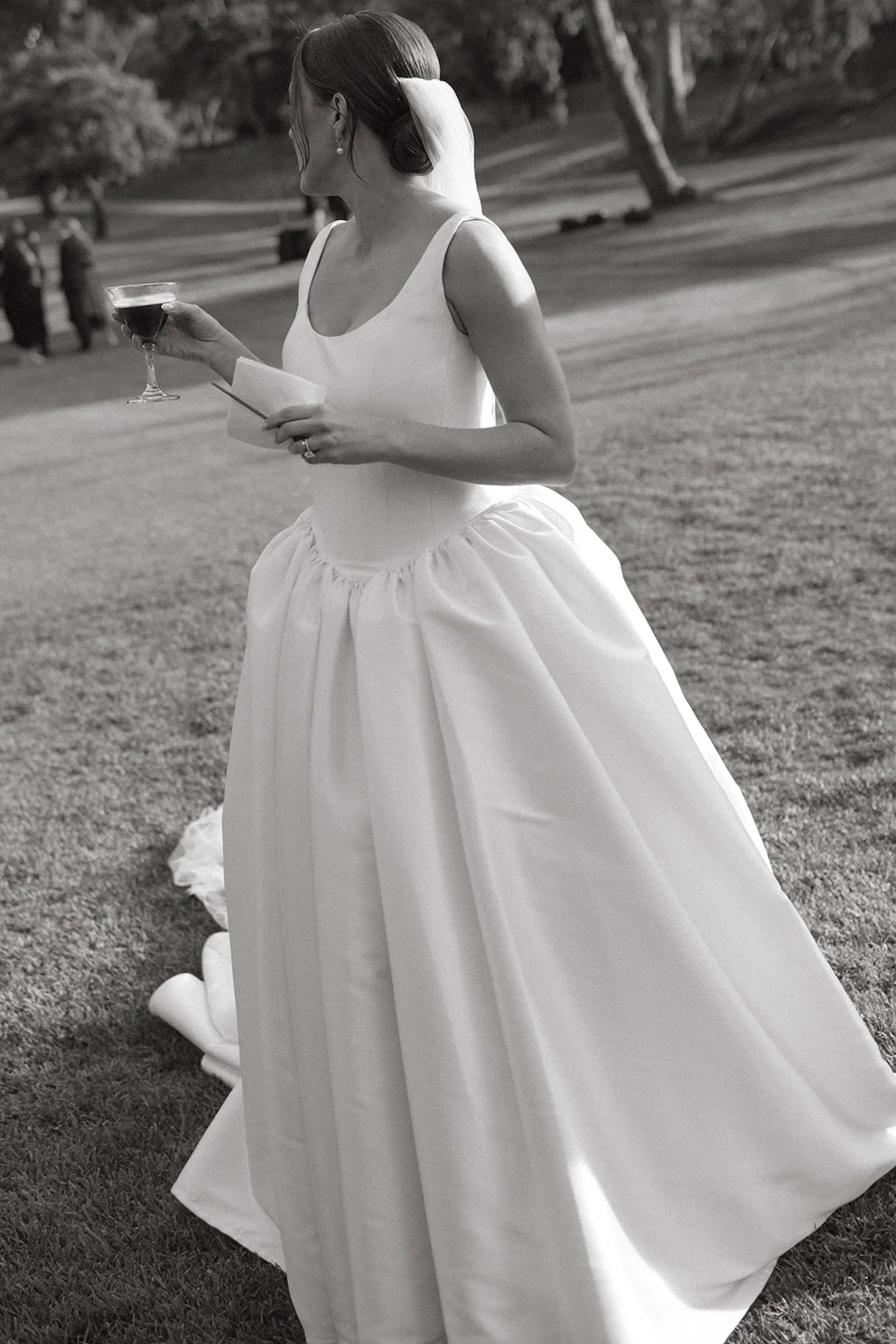 Bride holding a cocktail and paper note during reception candid moments on the lawn.