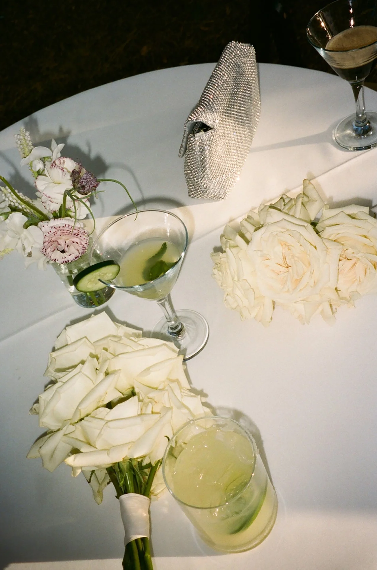 A film detail photo of the brides white rose bouquet, drinks, and other wedding details laying out on the reception tables!