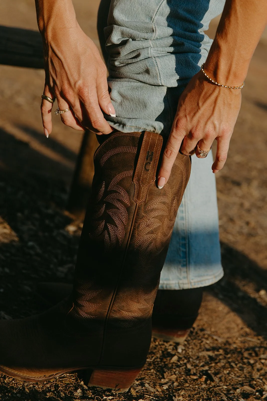 Detail shot of the bride adjusting her brown leather cowboy boots, engagement ring visible against denim jeans.