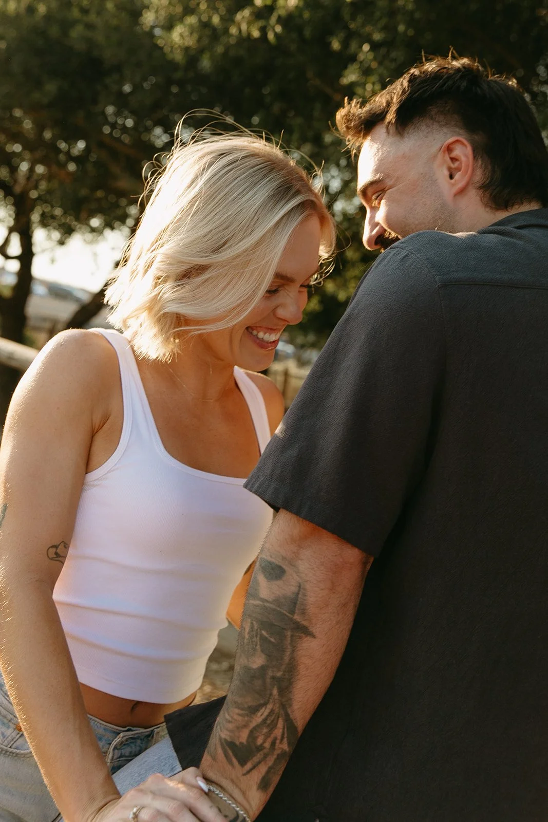 Playful western engagement photos of the couple laughing together in warm golden hour light, leaning into each other in a rustic field setting.