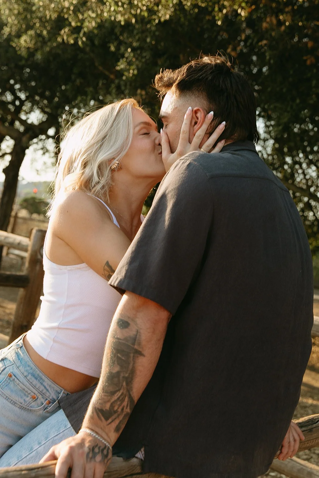 Playful western engagement photos of the couple kissing in warm golden hour light, leaning into each other in a rustic field setting.