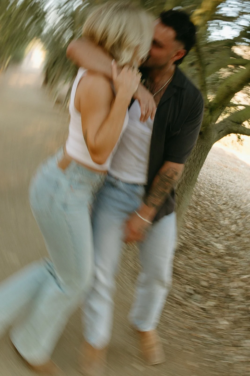 Lifestyle western engagement photos of the couple laughing together while walking under tree cover along a rustic path.