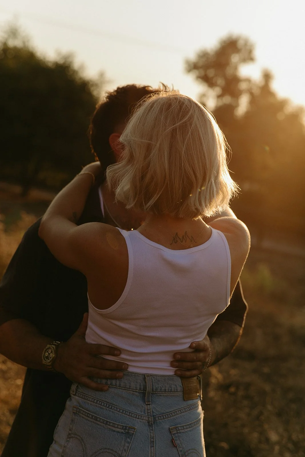 Backlit western engagement photos of the couple hugging and kissing in a golden field with sun flare behind them.