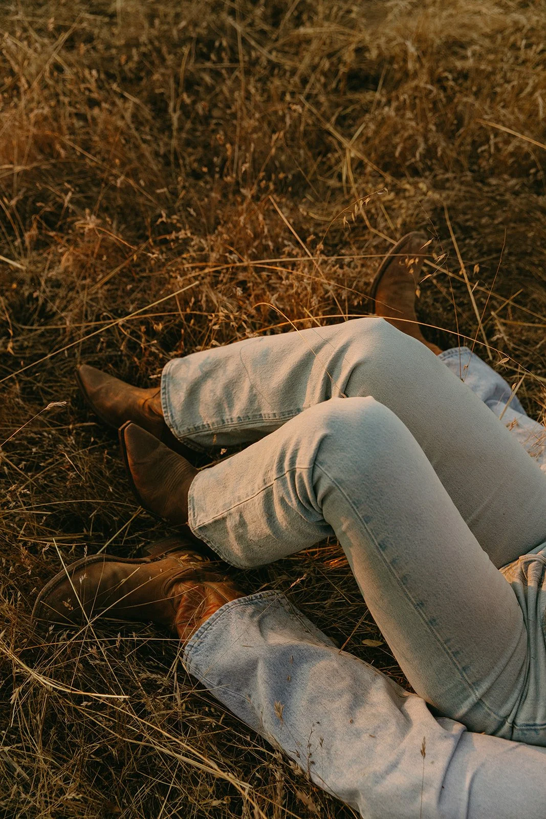 Scenic western engagement photos of the couple sitting together in a grassy field with mountains rising in the background.