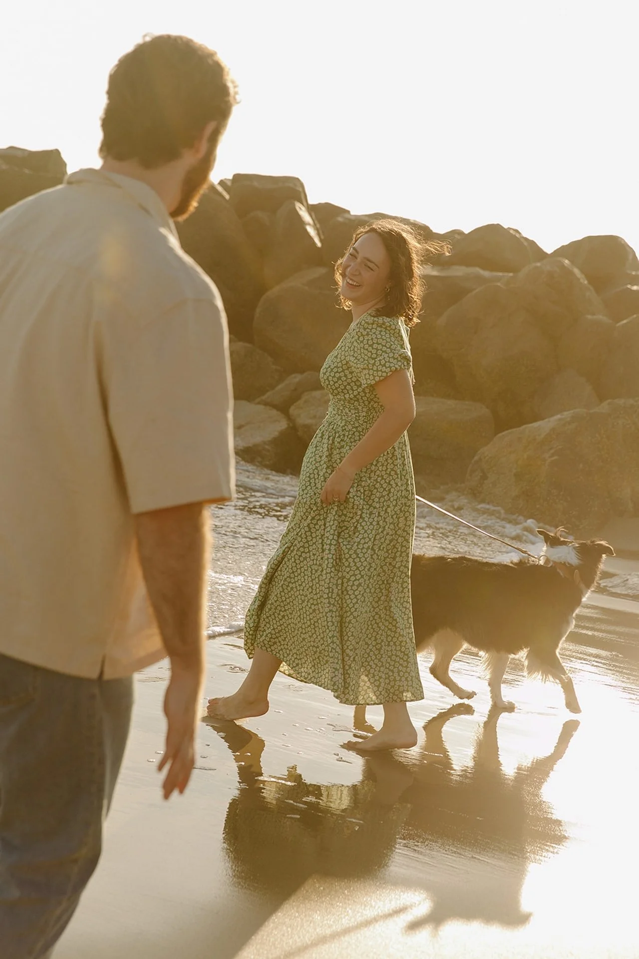 Sunset moment during their newport beach engagement photos as the couple walks along the beach with their dog near the rocky jetty.