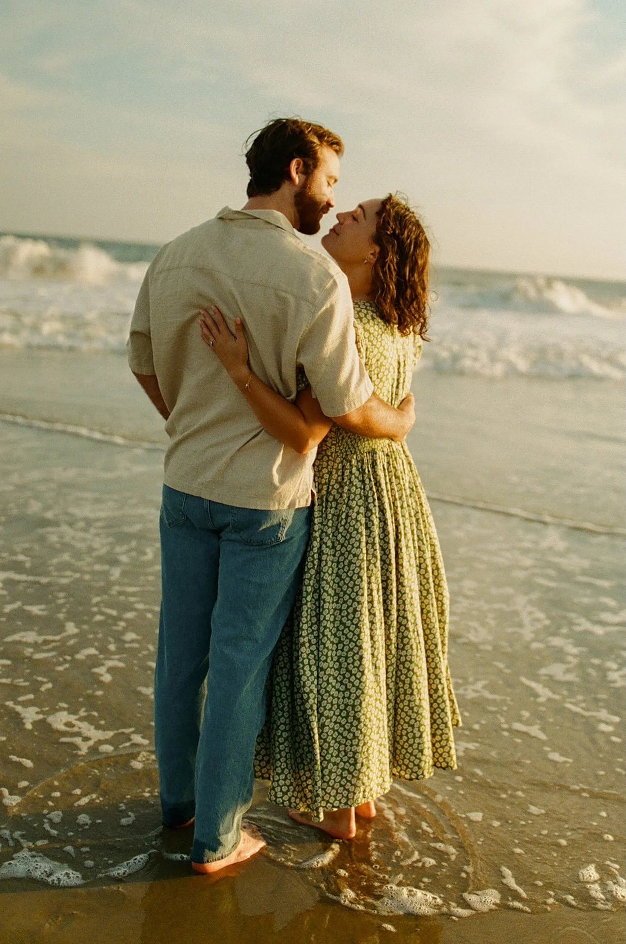 Romantic portrait from behind of a couple embracing in the ocean during their newport beach engagement photos as waves crash around their feet.