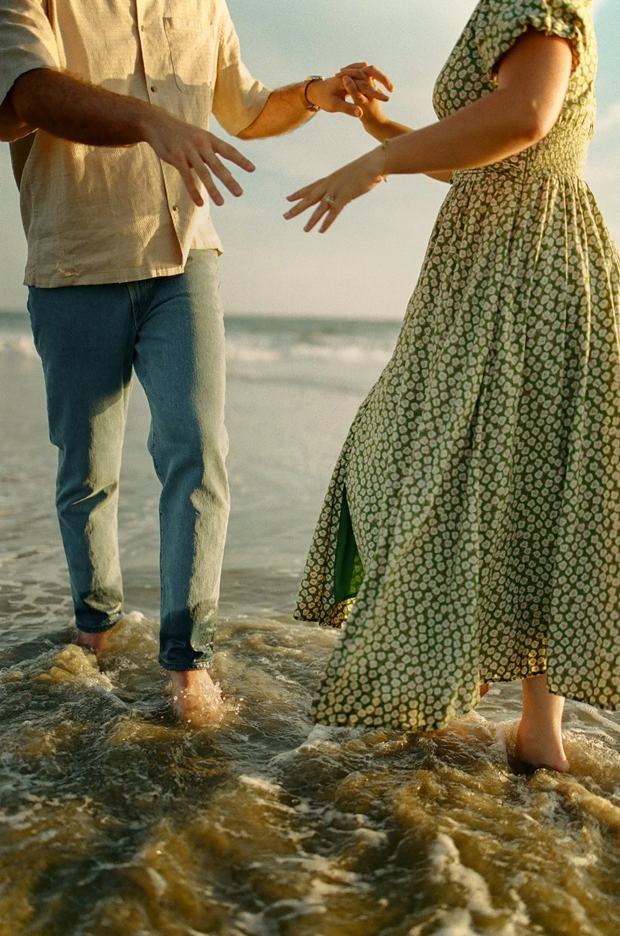 Candid photo of a couple holding hands at sunset during their newport beach engagement photos, golden light flaring around them as waves roll in behind.