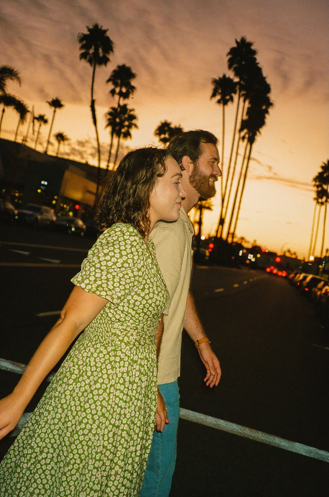 A candid photo of a couple walking across the street with the sunset behind them.