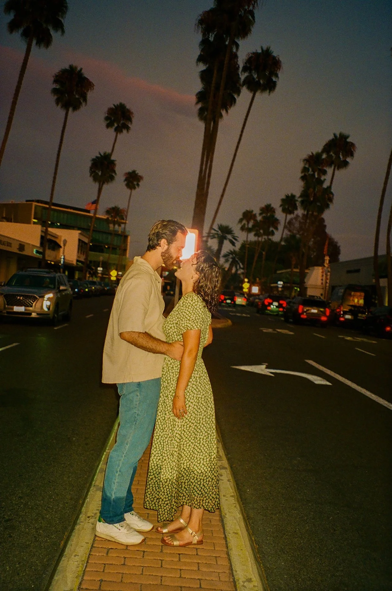 A romantic photo of a couple standing in the middle of the road leaning into each other at sunset.