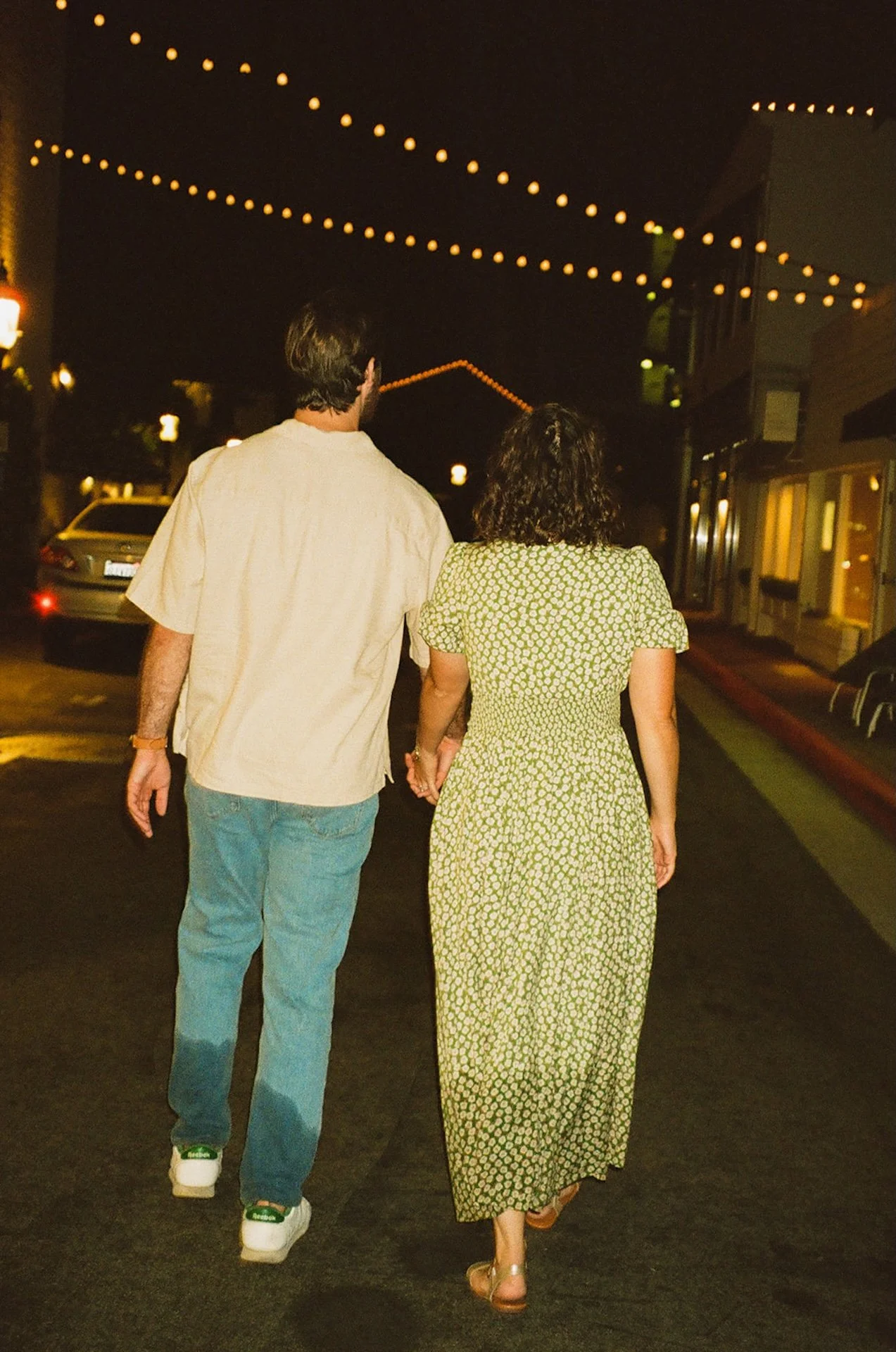 A couple walking hand in hand downtown in Lido Village after sunset during their newport beach engagement photos.