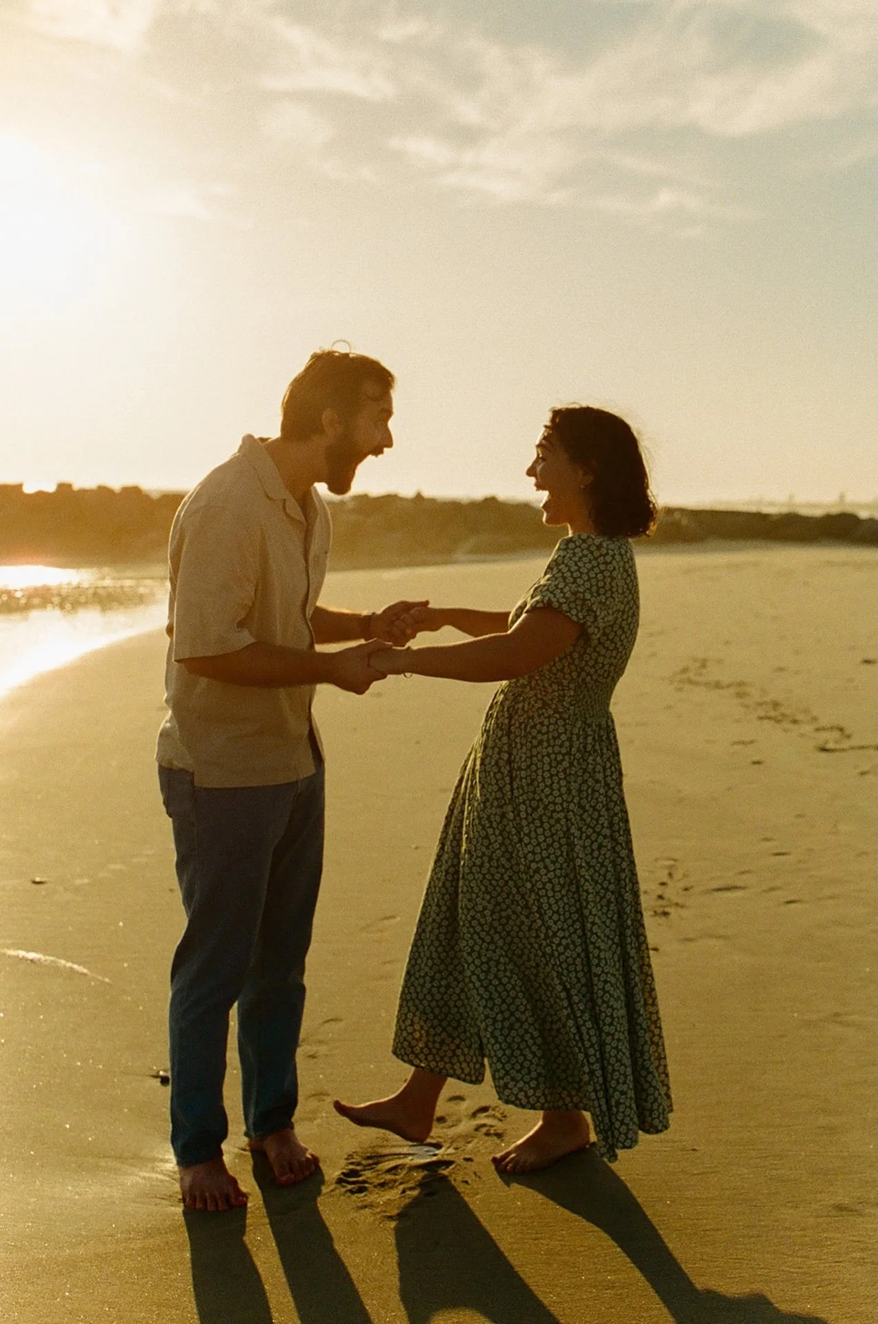 A fun candid photo of a couple holding hands and laughing together while walking around on the beach during their newport beach engagement photos