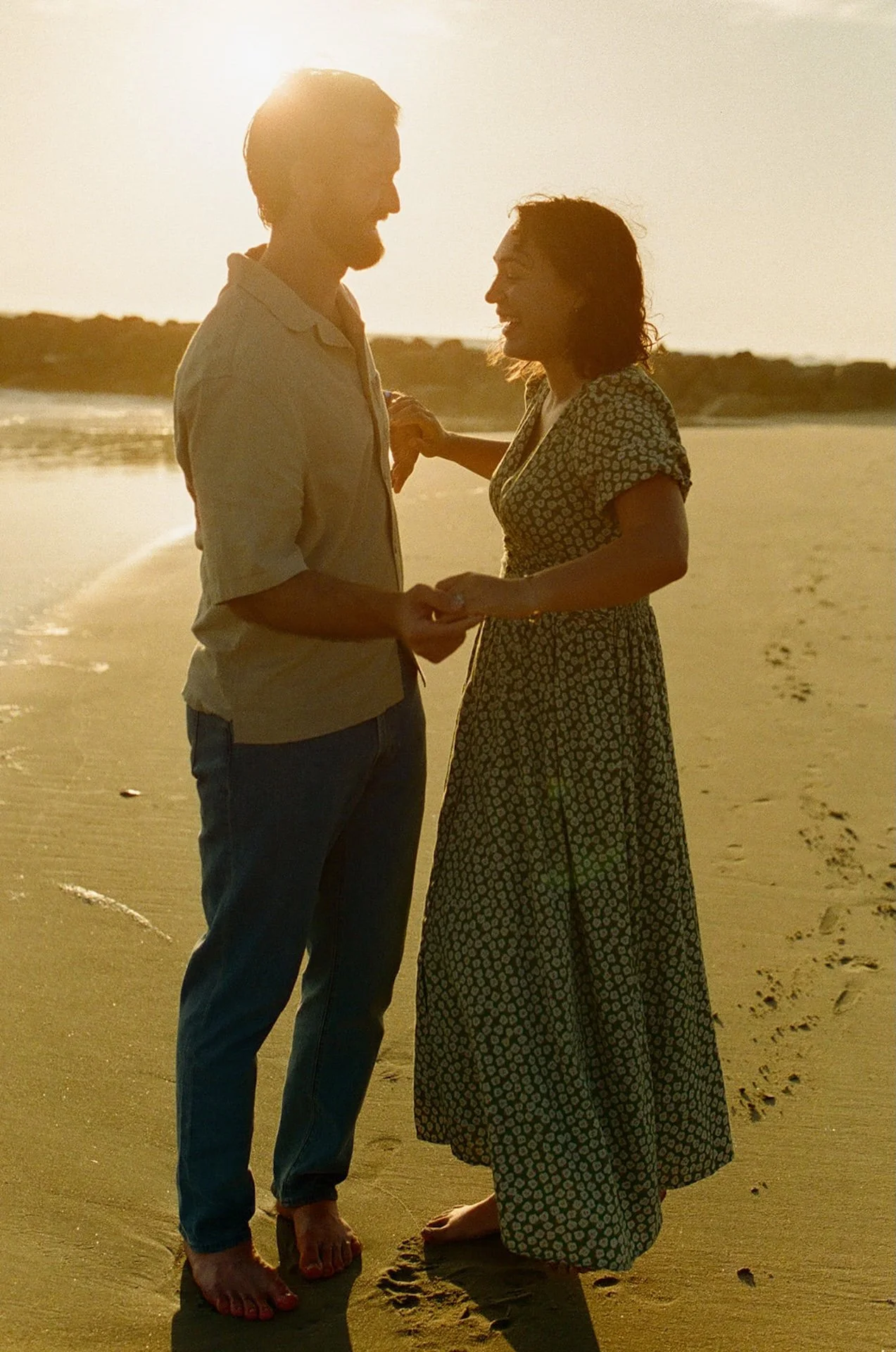 A fun candid photo of a couple holding hands and laughing together while walking around on the beach during their newport beach engagement photos