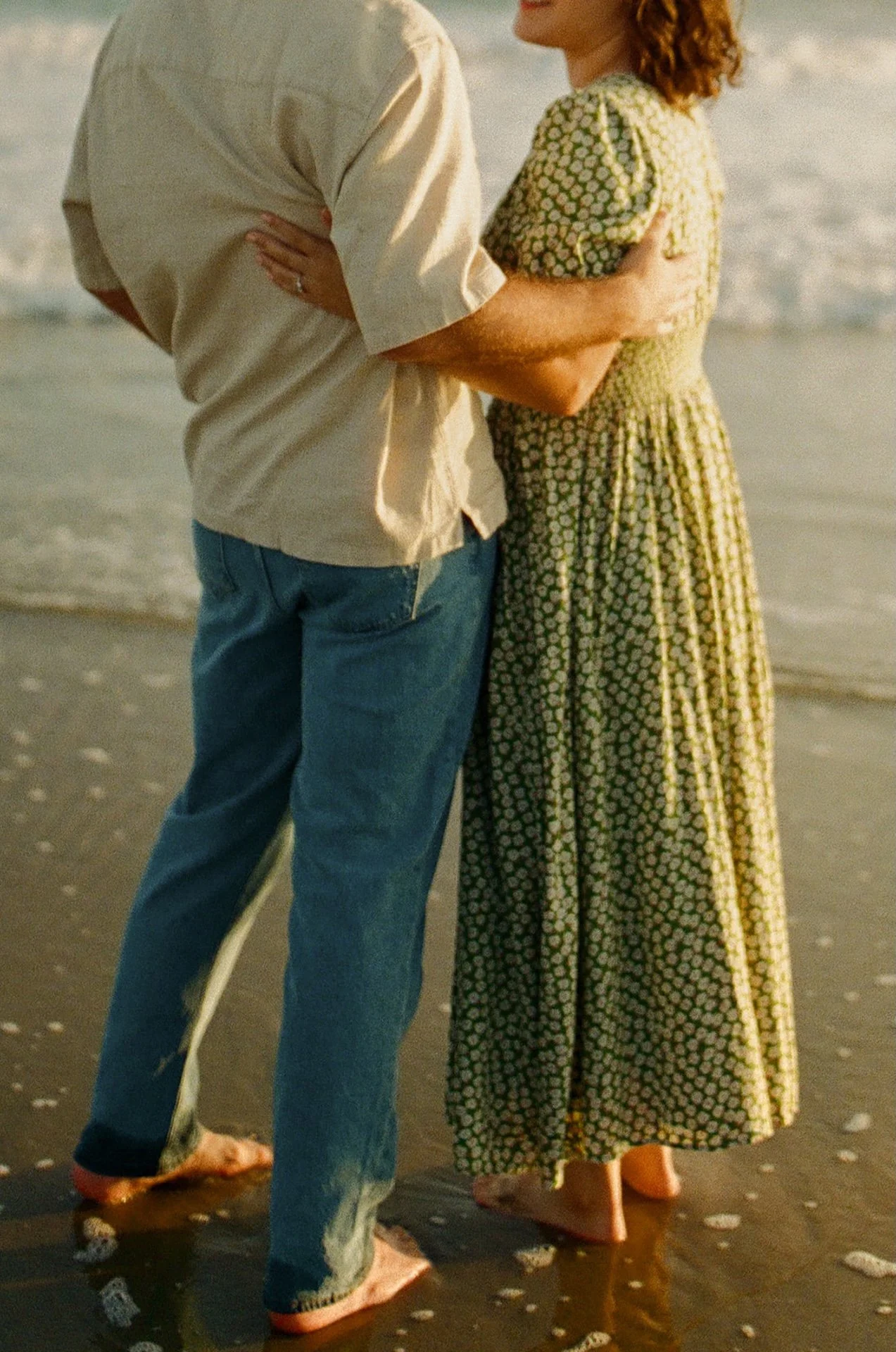 A candid photo of a couple hugging each other and smiling together while standing on the beach during their newport beach engagement photos