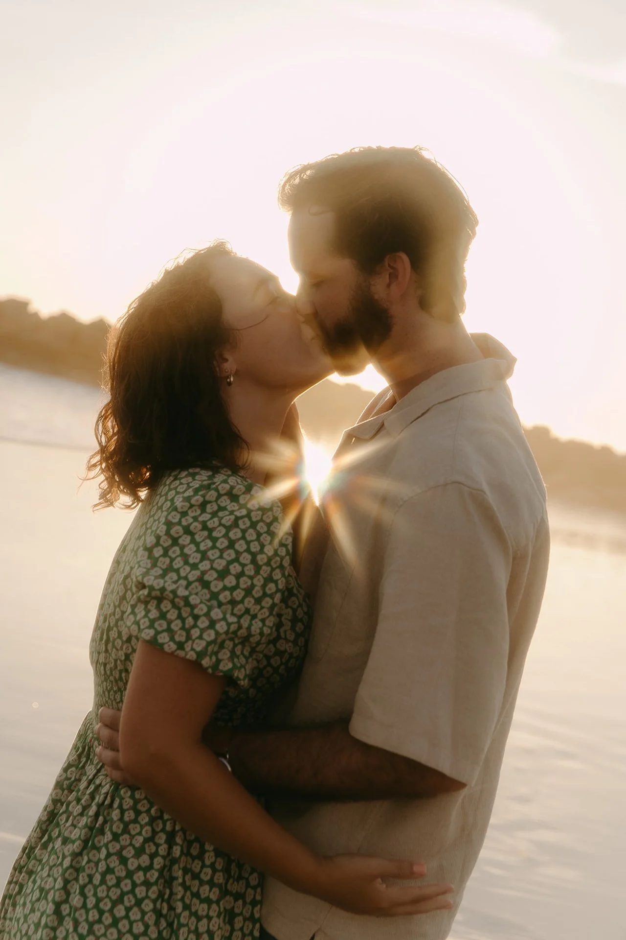 An artistic film photo of a couple sharing a kissing on the beach during their newport beach engagement photos with a sunflare glowing between them