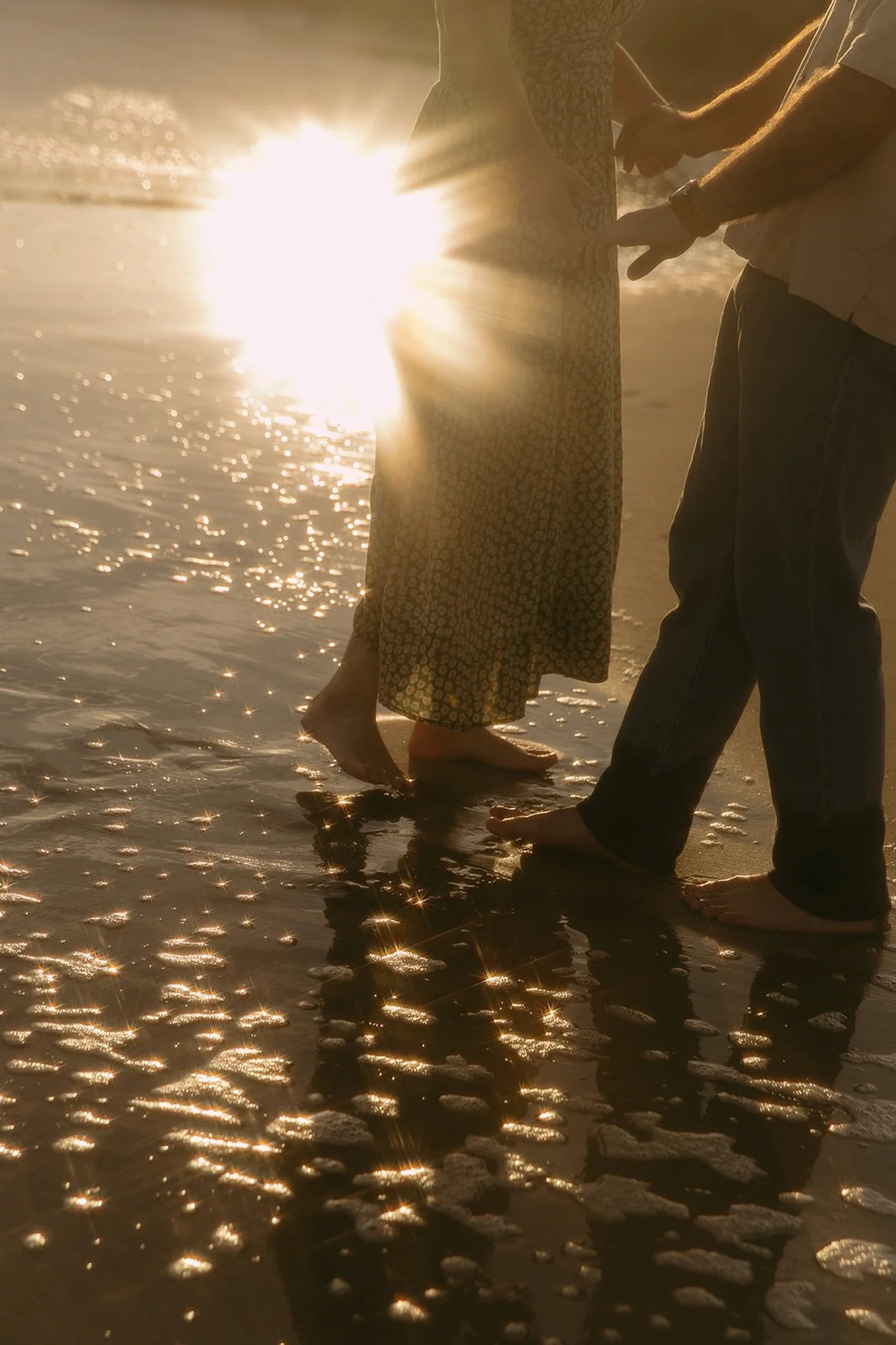An artistic film photo of a couple holding hands on the beach during their newport beach engagement photos with a sunflare behind them