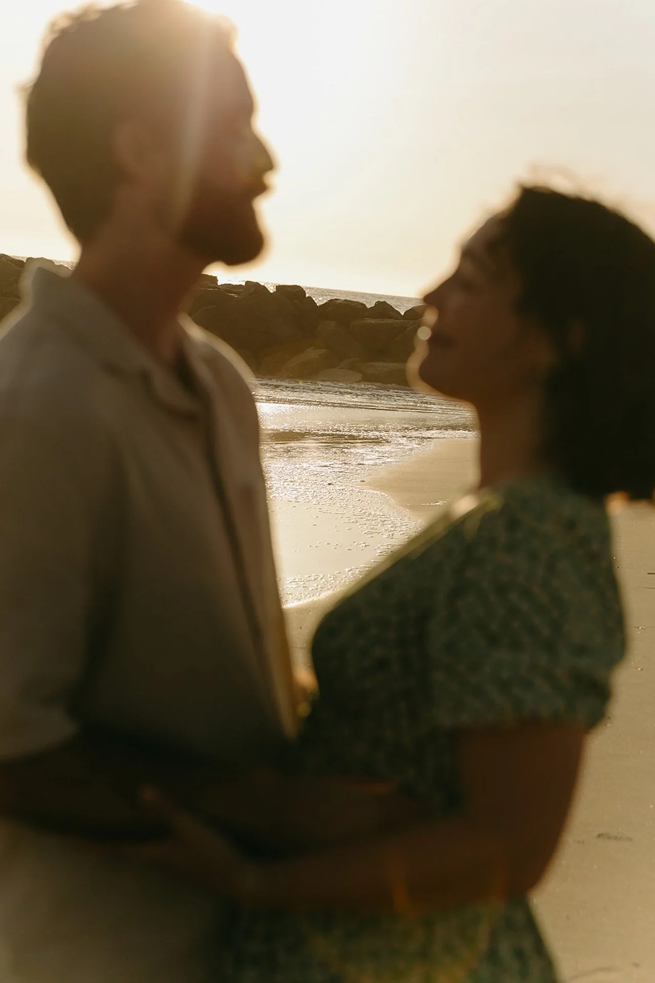 A blurry candid photo of a couple hugging and looking at each other during their beach engagement shoot at sunset.