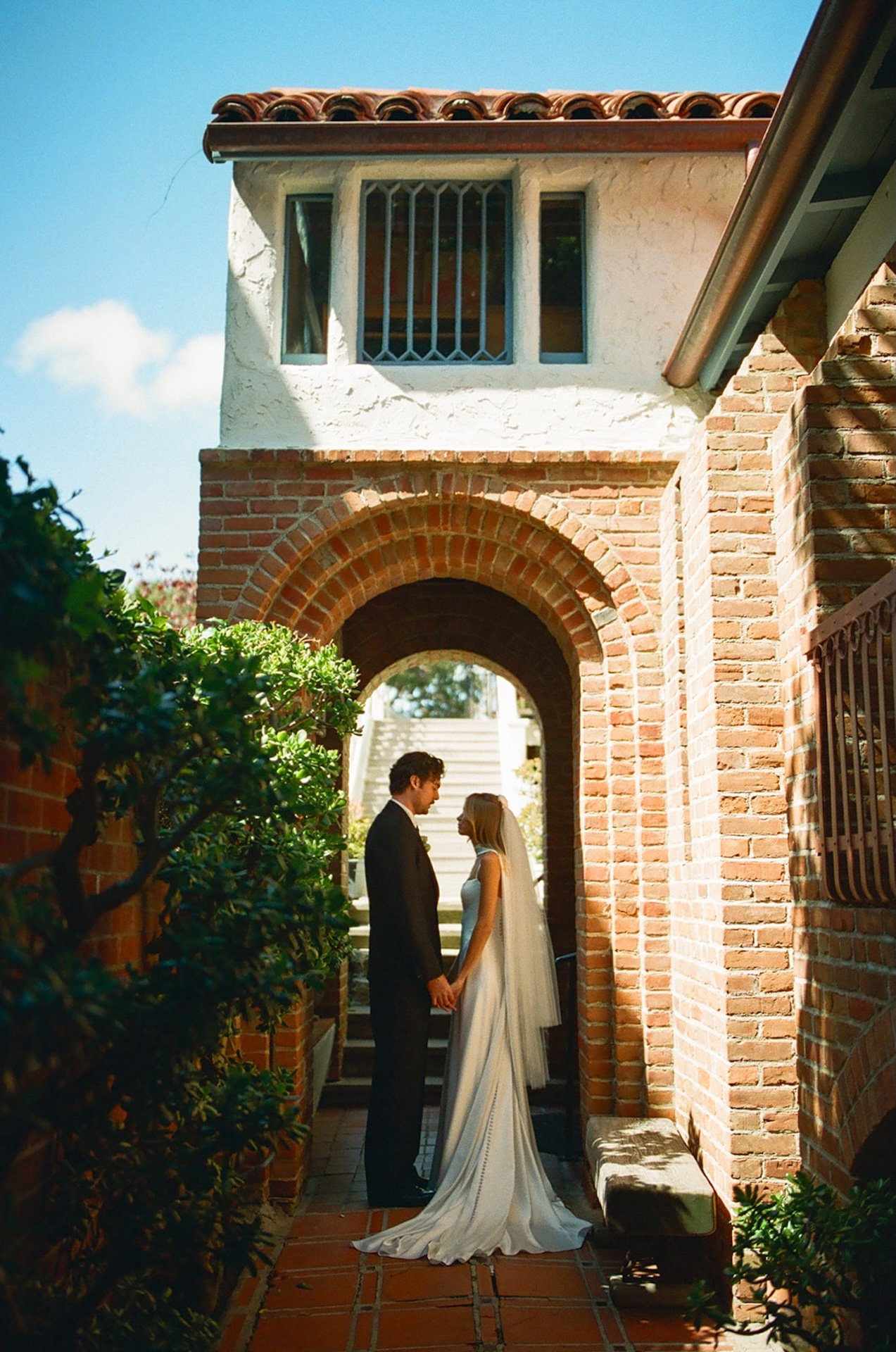 Bride and groom standing together beneath a brick archway at a historic church during their romantic Laguna Beach wedding portraits.