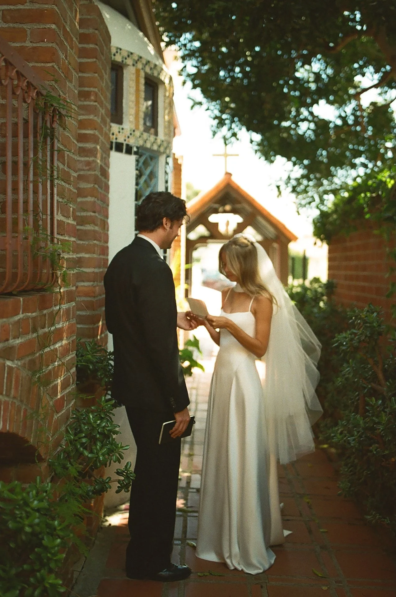 Bride and groom read handwritten vows together in a quiet brick courtyard beside a Spanish-style church in Laguna Beach before their ceremony.