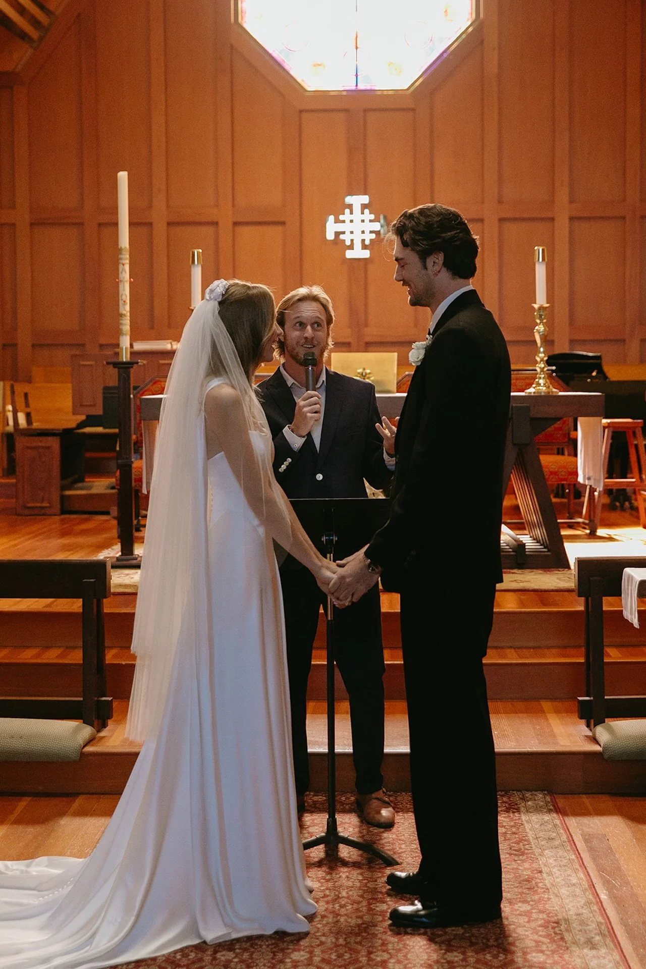Bride and groom holding hands while exchanging vows during their intimate Laguna Beach wedding ceremony inside a wooden church.