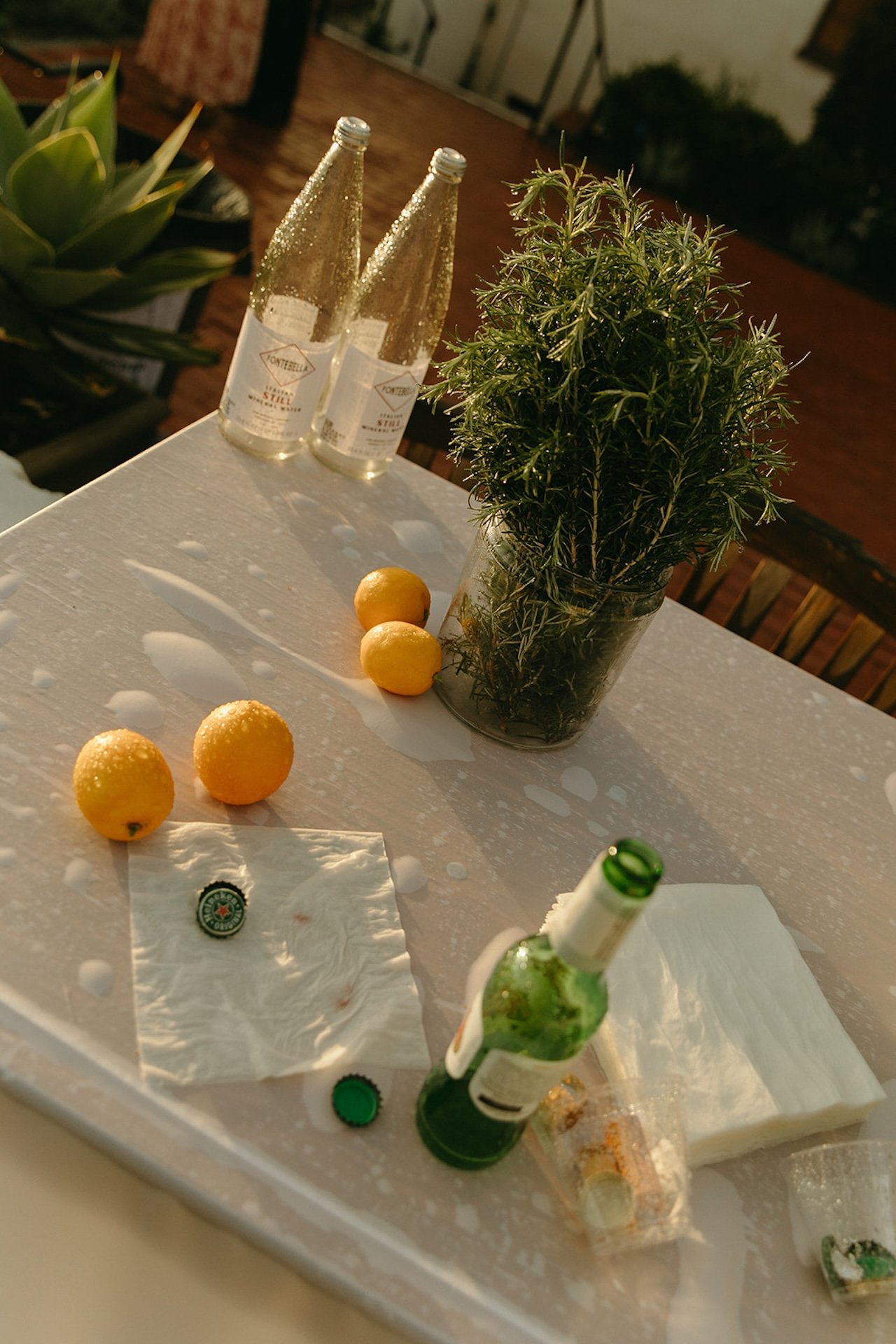 Reception table still life with sparkling water bottles, lemons, herbs, and drinks glowing in warm evening light at a Laguna Beach wedding celebration.