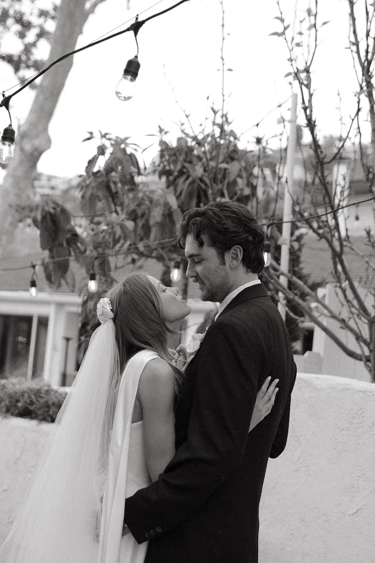 Bride and groom embracing beneath string lights during an intimate black and white Laguna Beach wedding portrait.