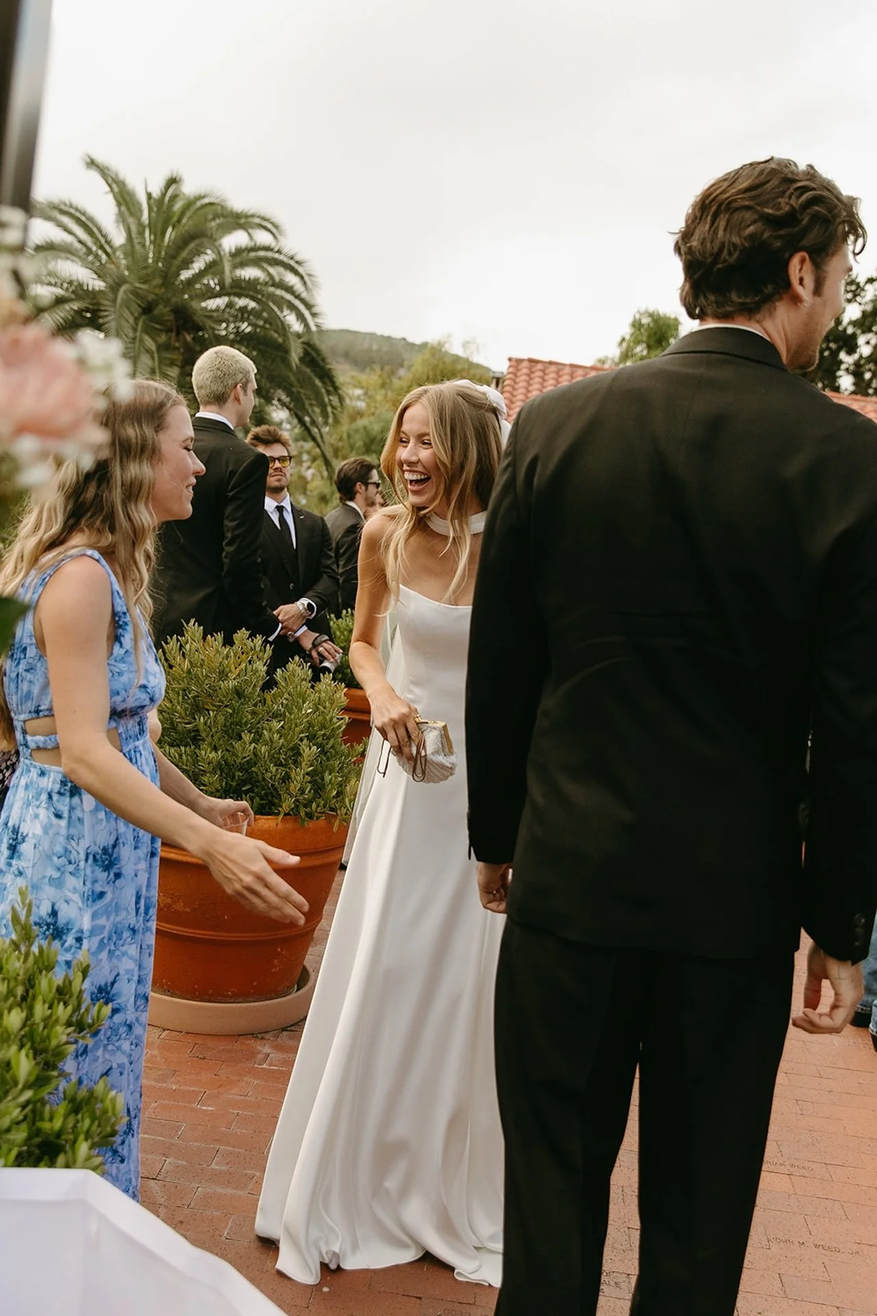 Bride smiling and greeting guests during cocktail hour at an outdoor terrace Laguna Beach wedding reception.