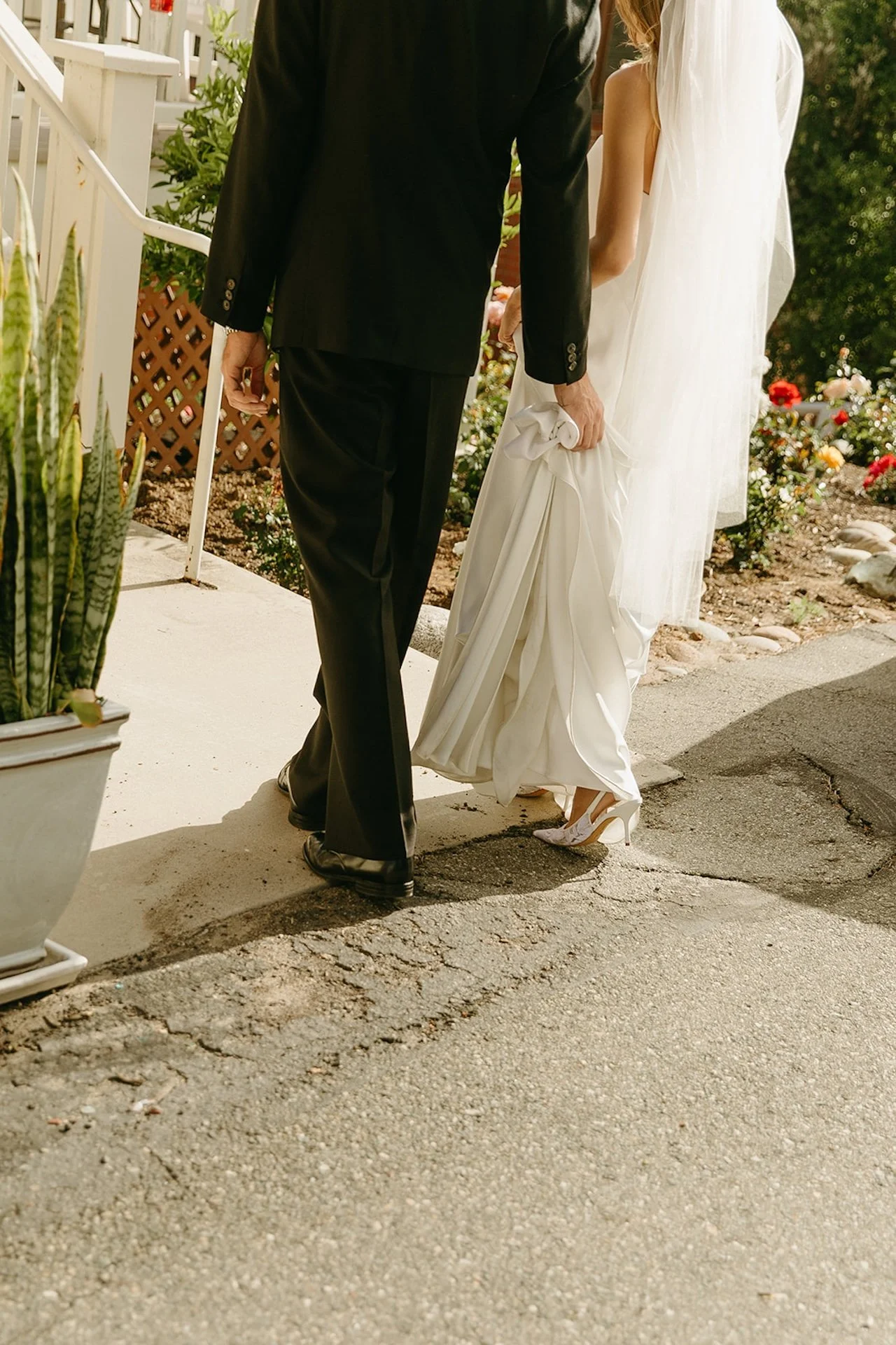 Close-up of the bride holding up her wedding dress while walking beside the groom outside the church.