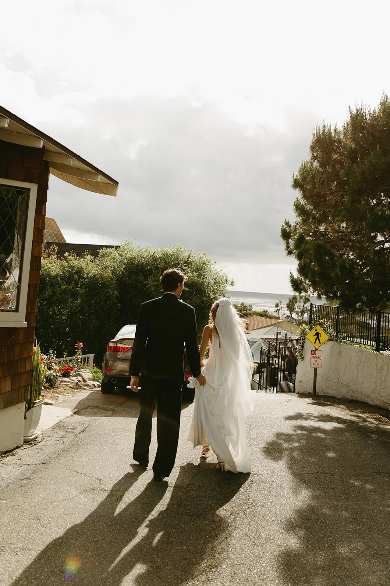 Newly married couple walking hand in hand down a hill toward the ocean after their Laguna Beach wedding ceremony.