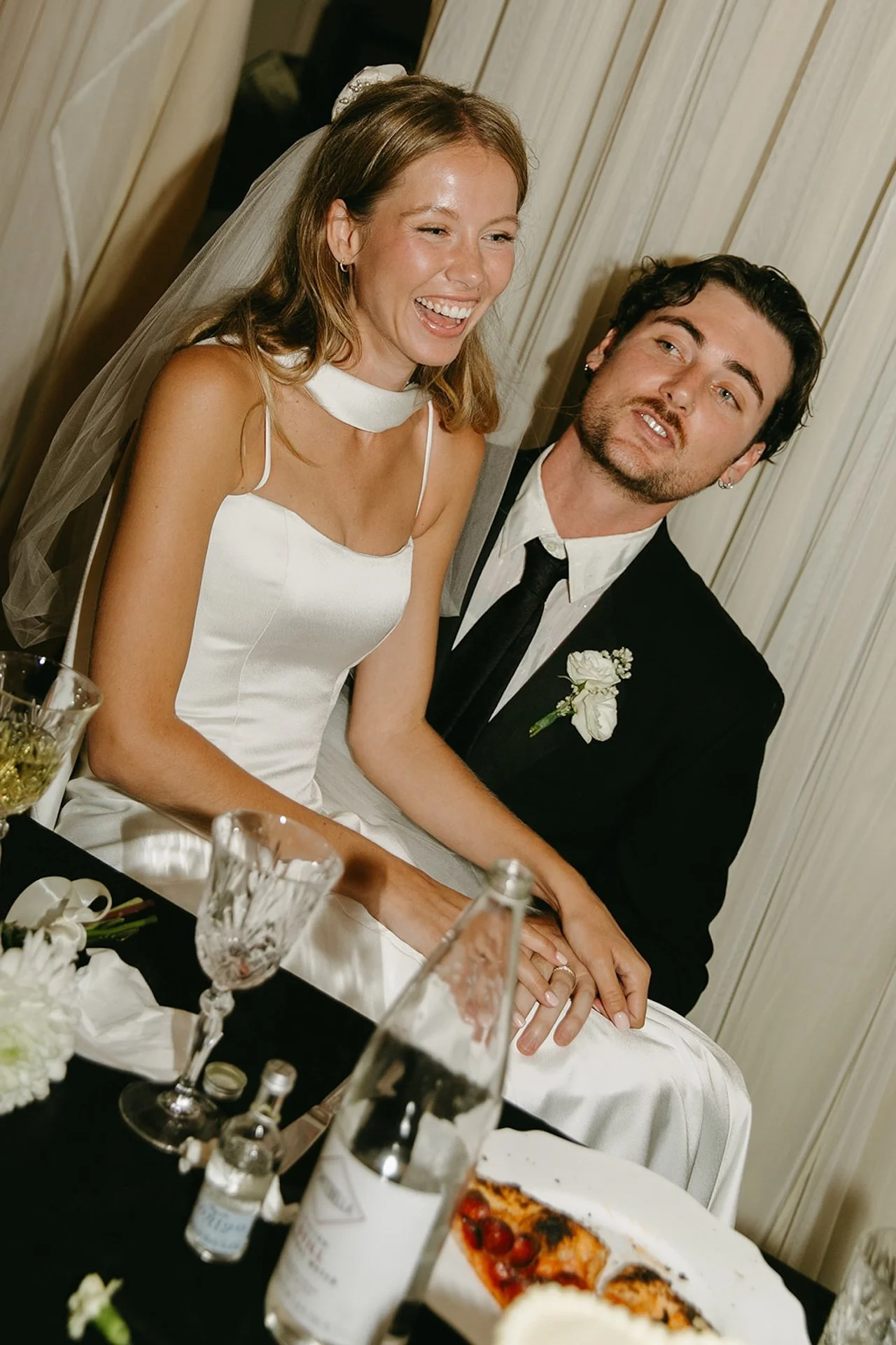 Bride and groom laughing together while seated at their reception table surrounded by wine glasses and candlelight during their Laguna Beach wedding celebration.