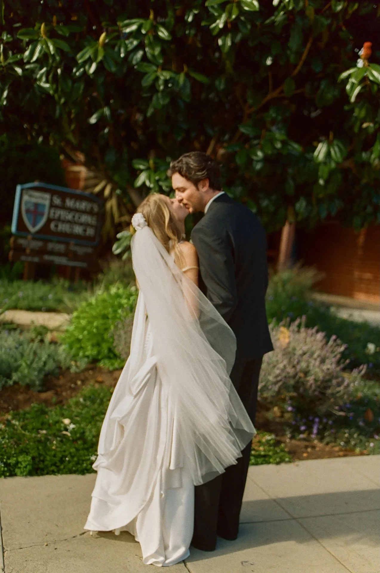Bride and groom sharing a quiet kiss in a lush garden outside St. Mary’s Episcopal Church in Laguna Beach.