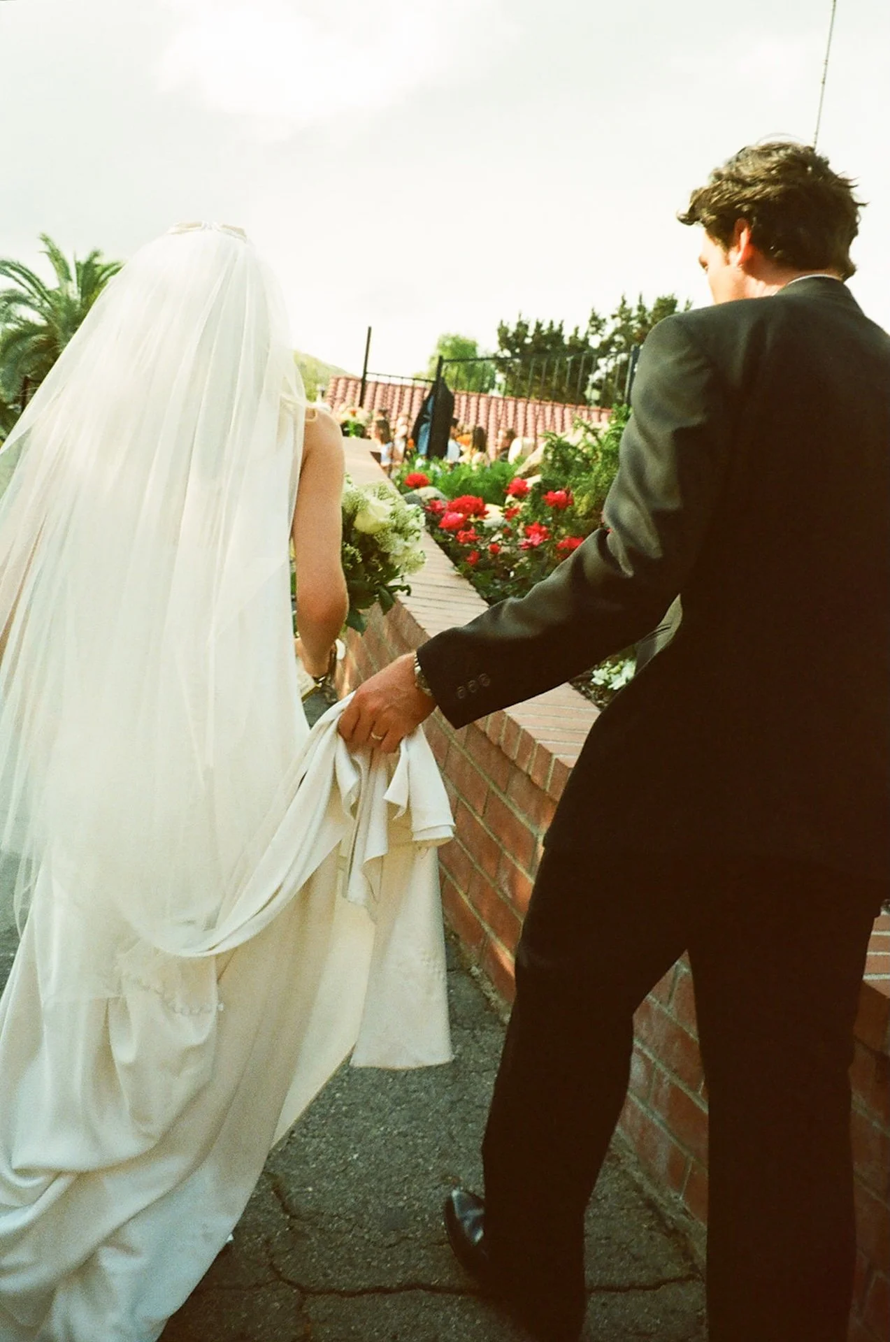 Newly married couple walking together toward their reception while the groom lifts the bride’s dress during their Laguna Beach wedding celebration.