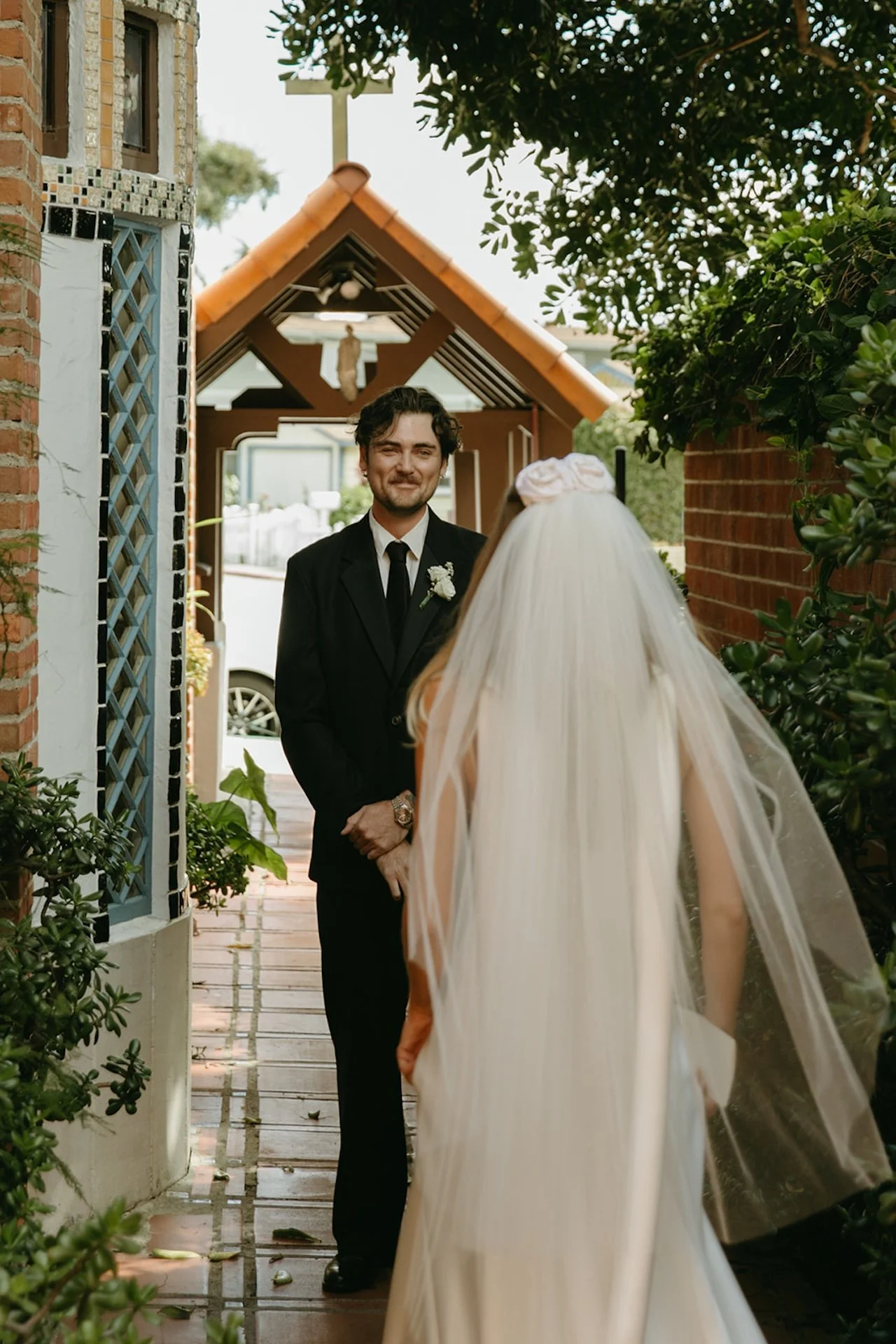 Groom smiling as the bride approaches for their first look along a garden walkway at their Laguna Beach wedding.