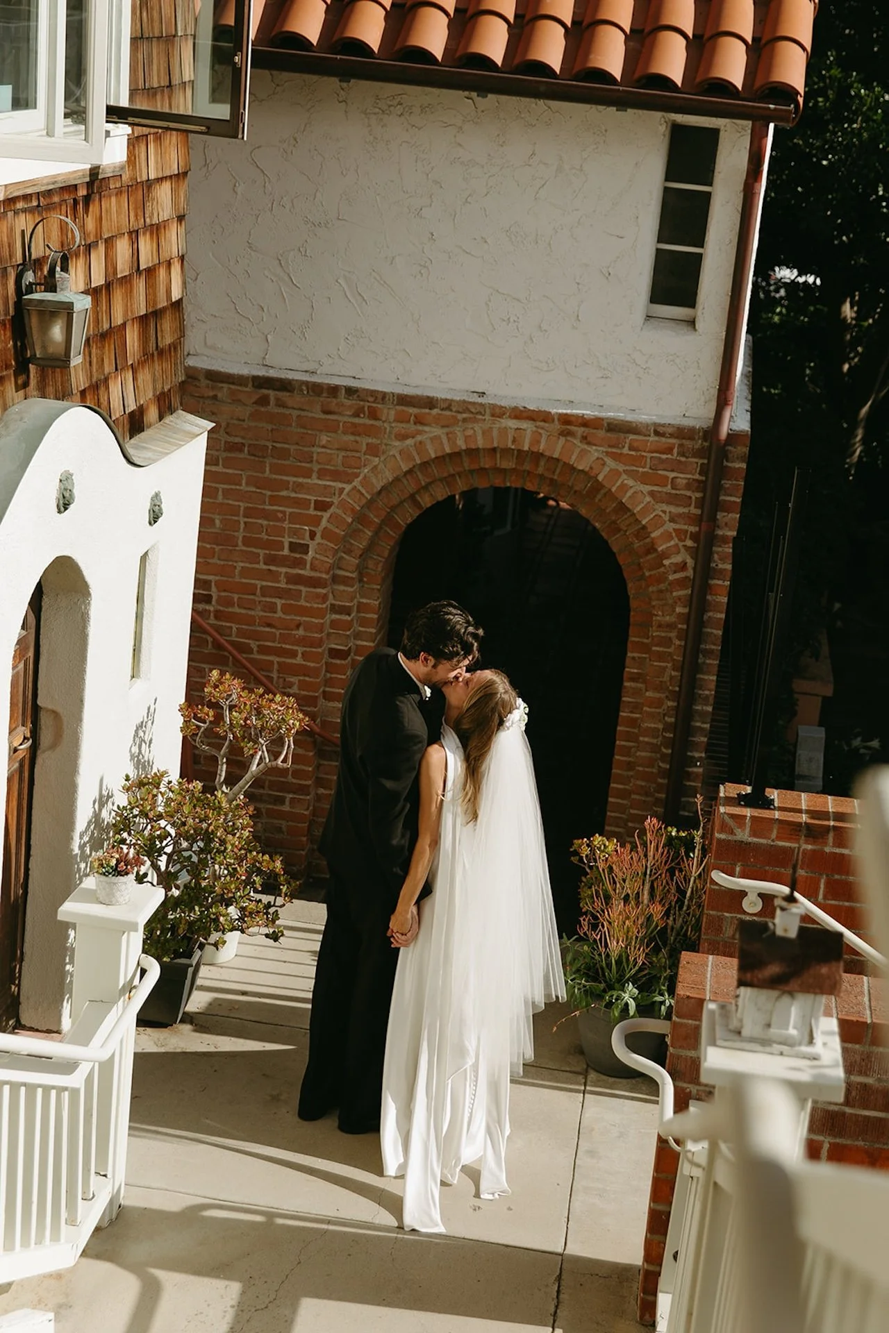 Bride and groom sharing a kiss beneath a brick archway outside the church courtyard.