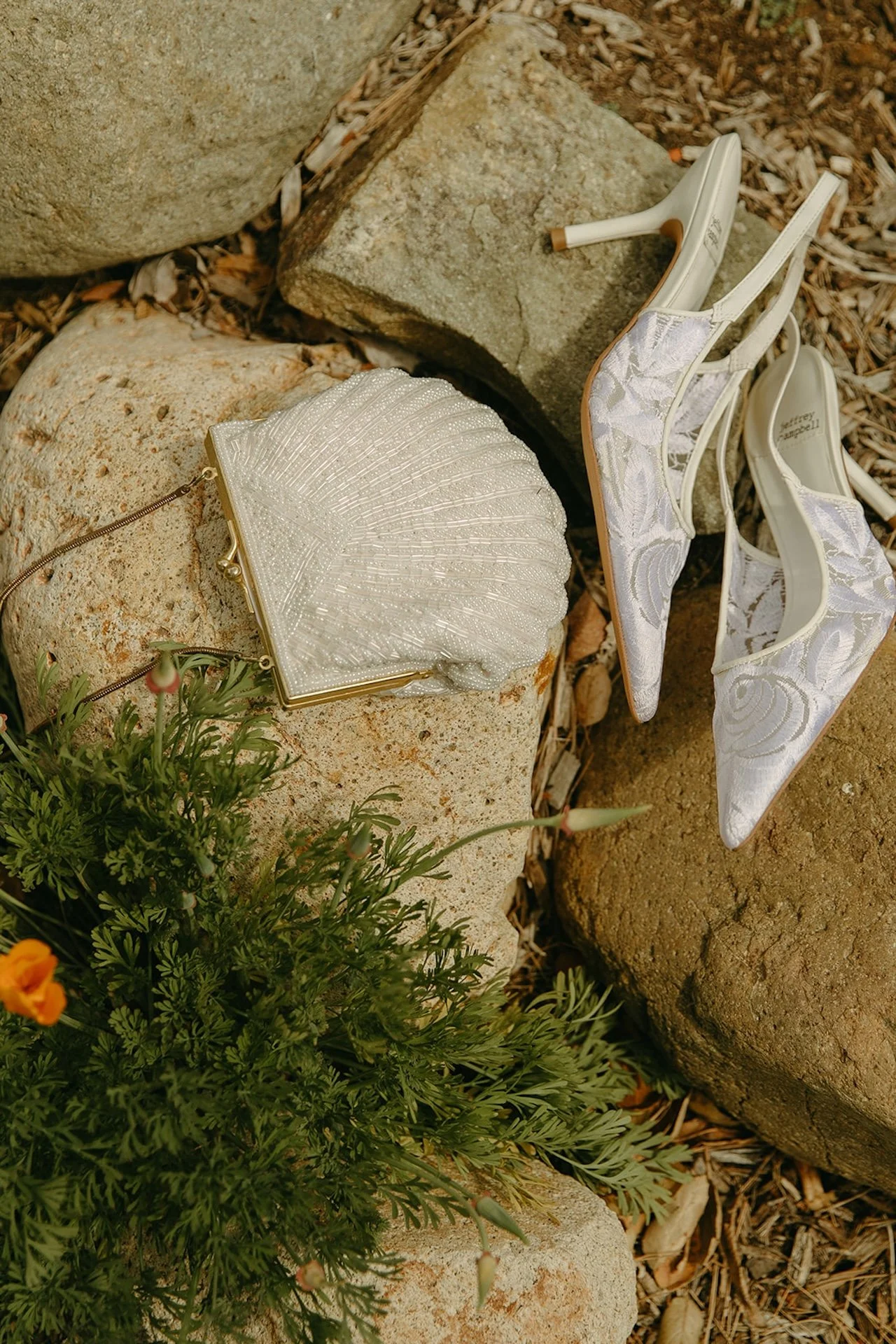 Wedding shoes and a beaded clutch styled on garden stones during bridal detail photos at a Laguna Beach wedding.