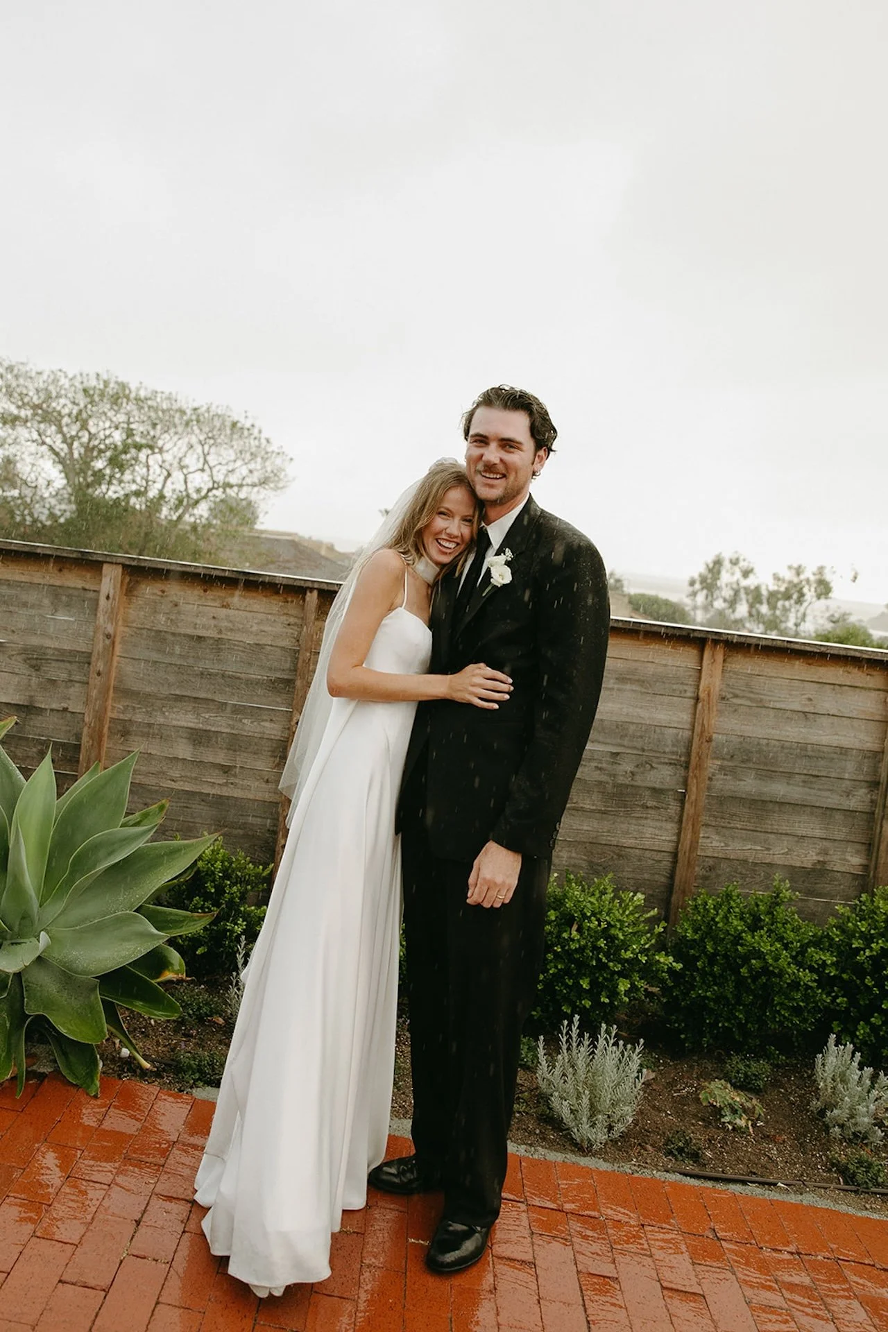 Couple hugging and smiling together outside during a rainy Laguna Beach wedding portrait.
