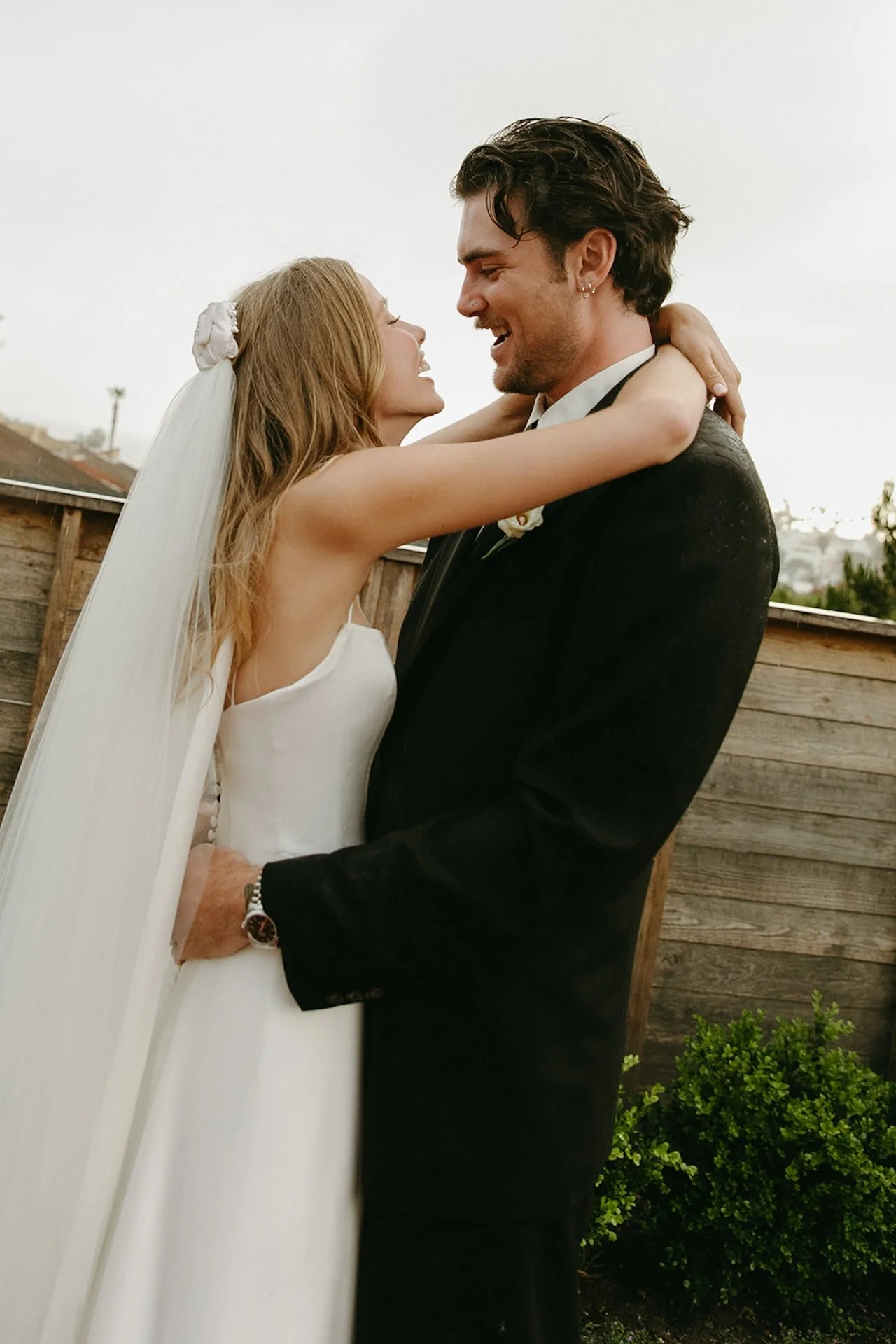 Bride and groom embracing and smiling at each other during romantic Laguna Beach wedding portraits in light rain.