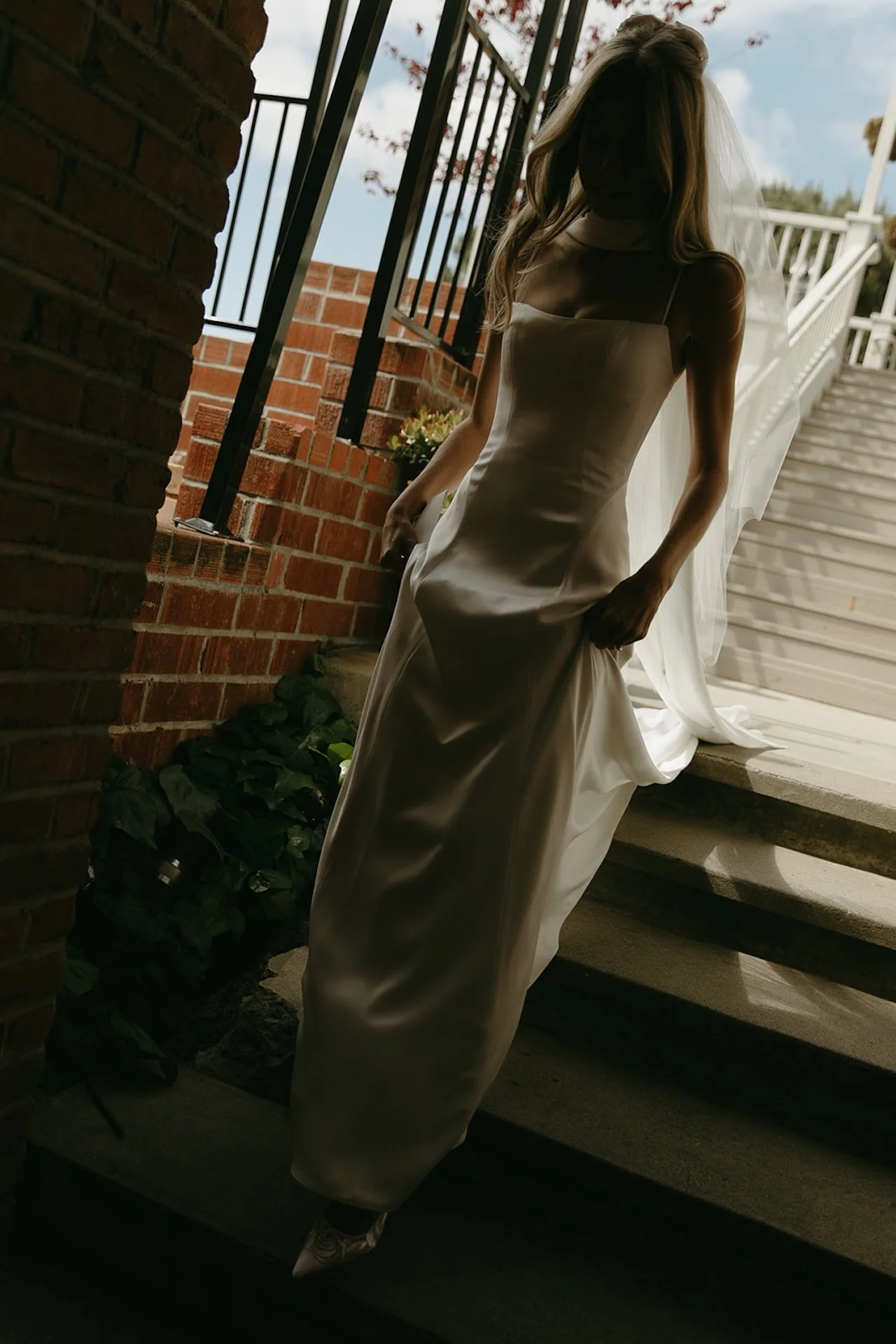 A candid photo of the bride holding her dress and walking down stairs before meeting her husband for their first look.