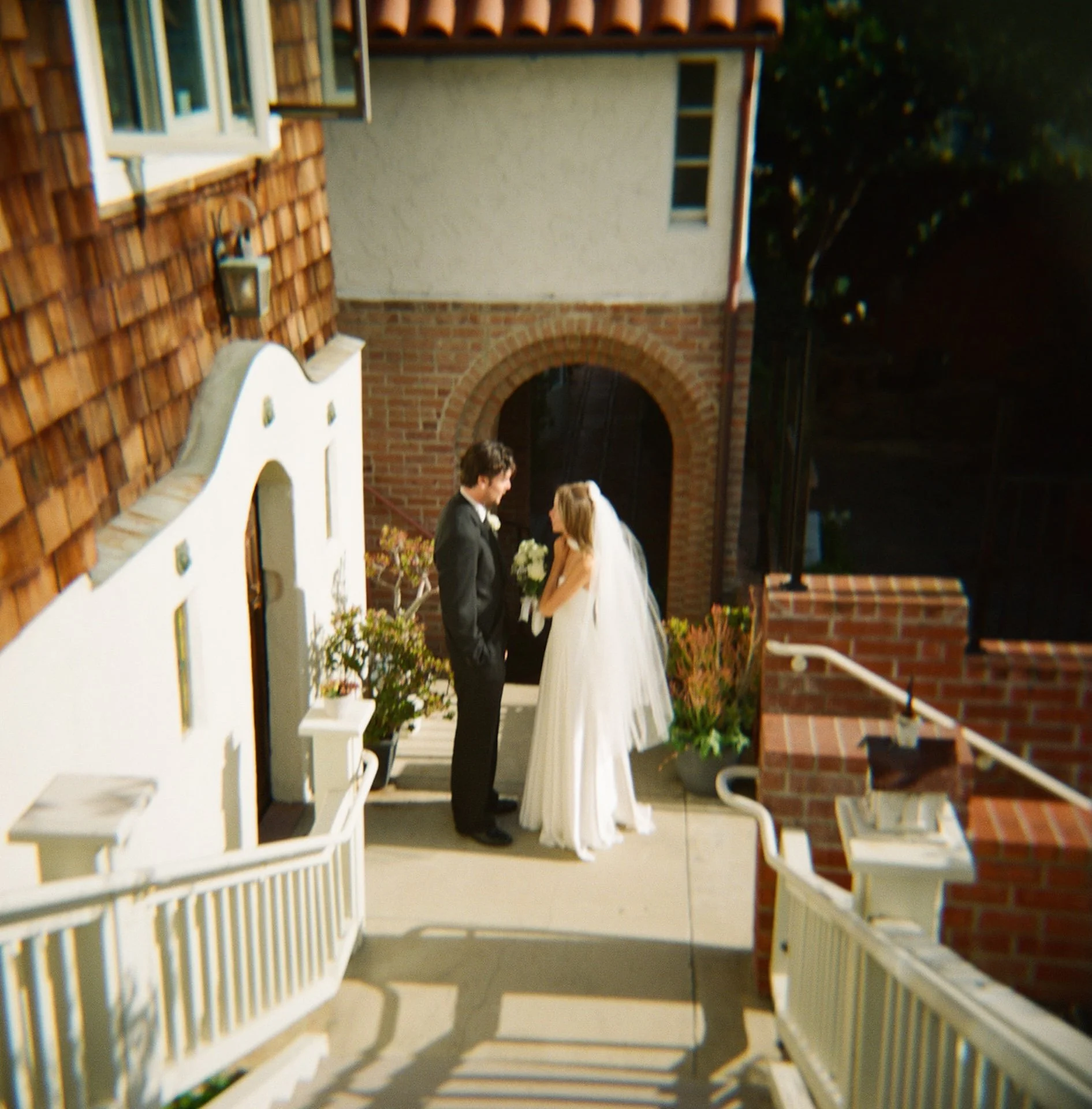 Bride and groom sharing a kiss beneath a brick archway outside the church courtyard.