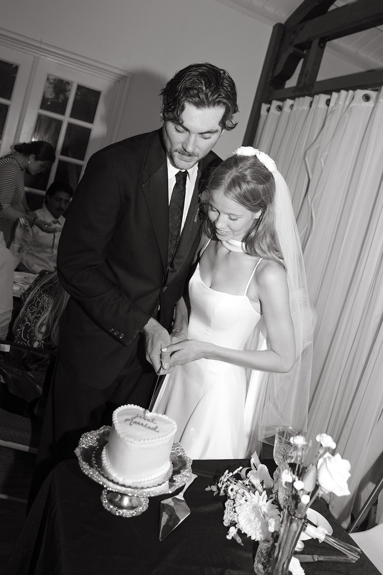 A black and white flash photo of the bride and groom cutting their cake that says "just married"